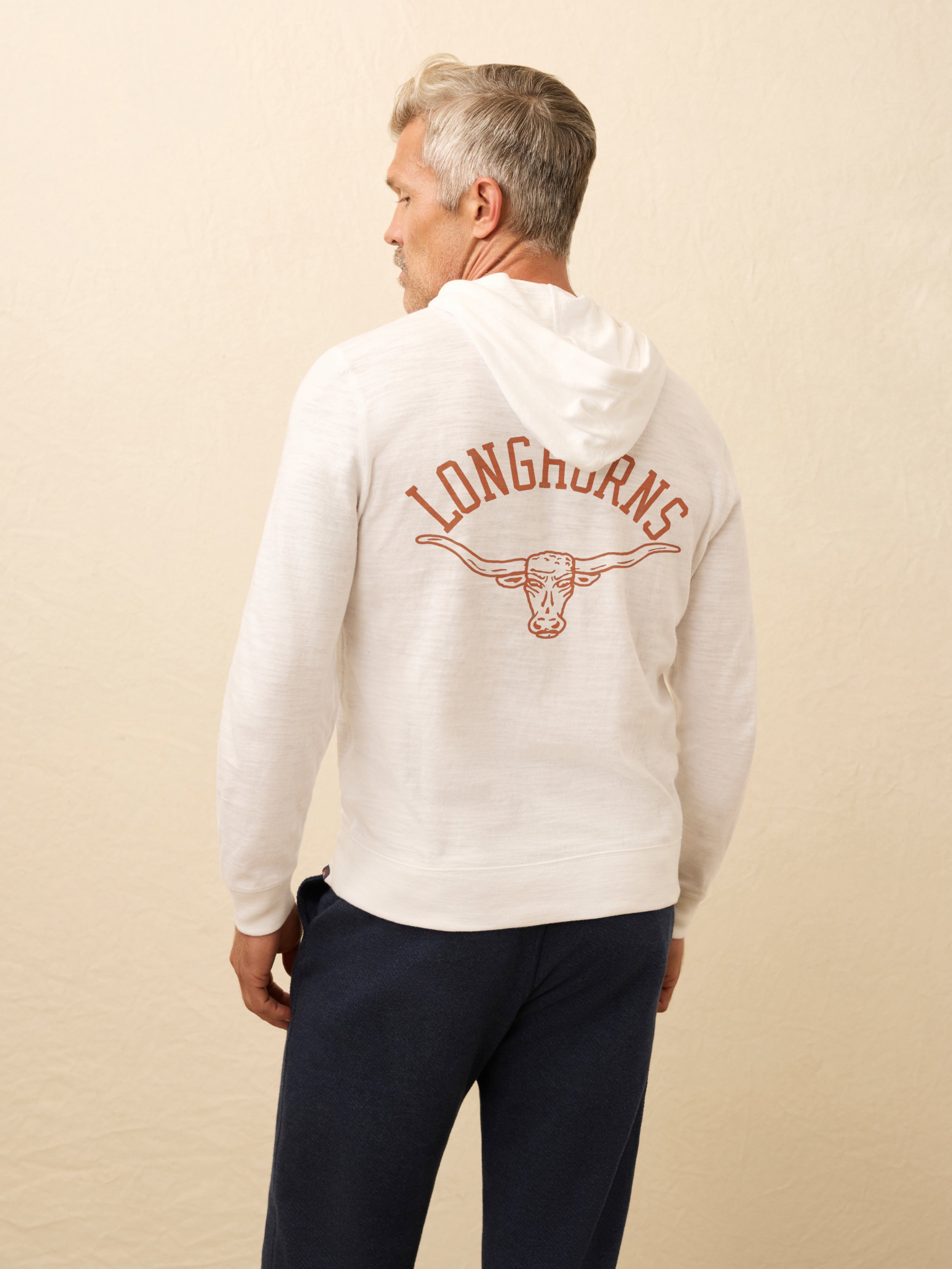 Man wearing a white hoodie with UT Austin graphic on the center back against a beige background