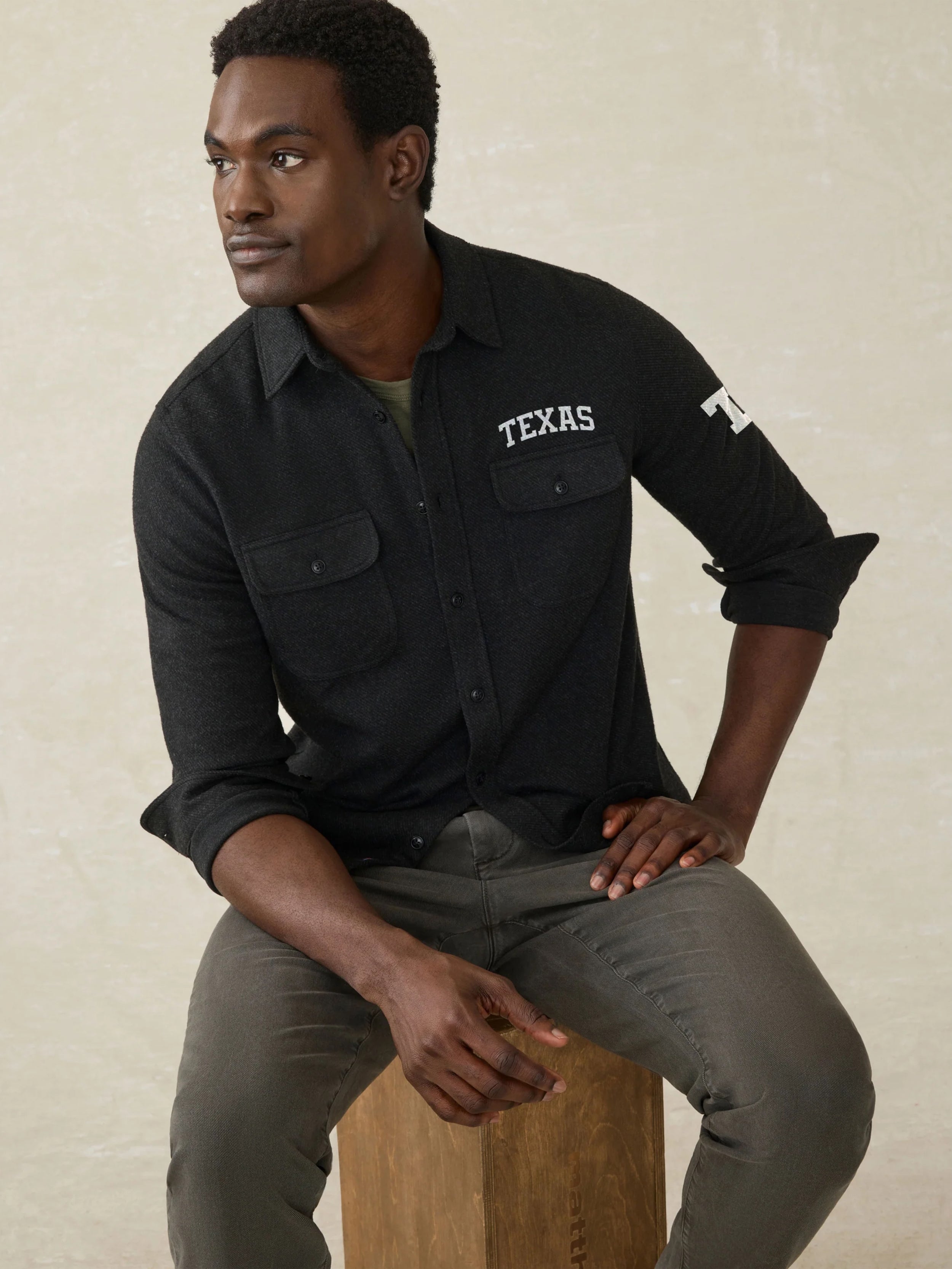 Man wearing a black long sleeve button up shirt with UT Austin graphic on the left check and shoulder against a beige background