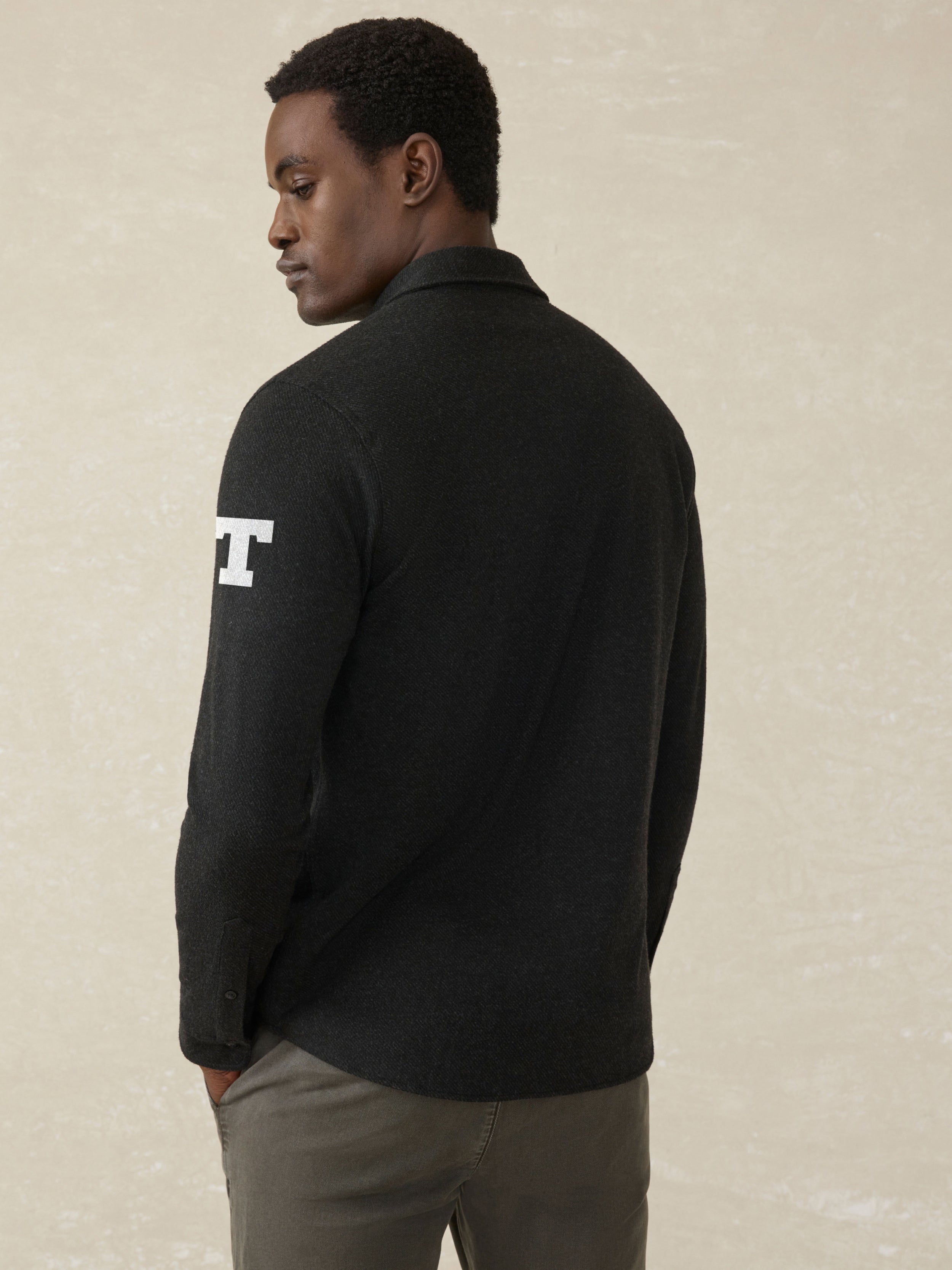 Man wearing a black long sleeve button up shirt with UT Austin graphic on the left check and shoulder against a beige background