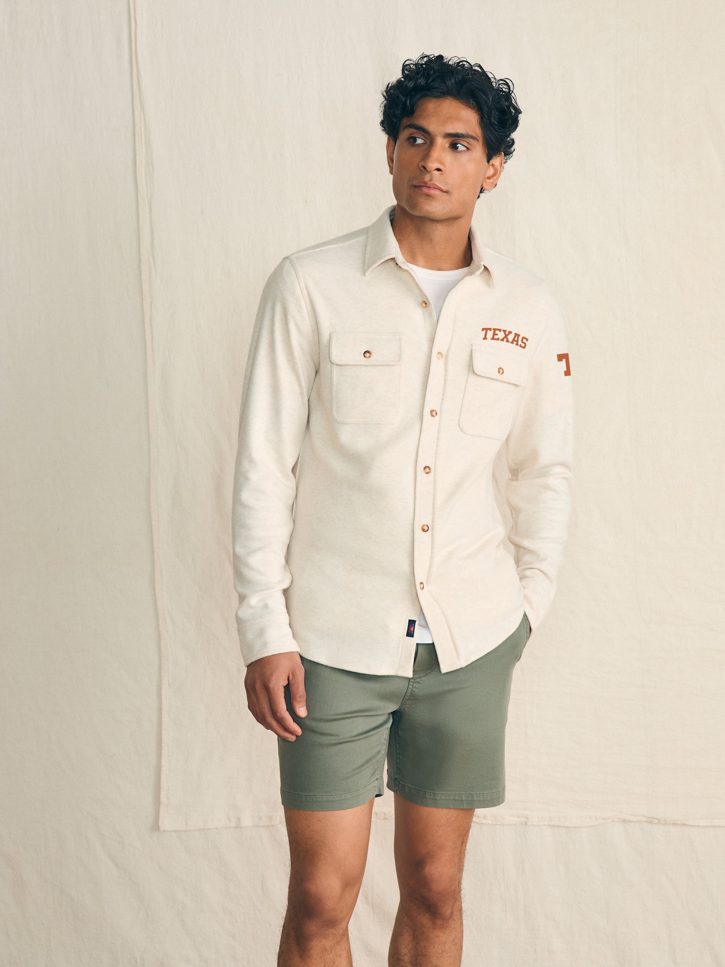 Man wearing a white shirt with UT Austin graphic on the left chest and shoulder against a beige background