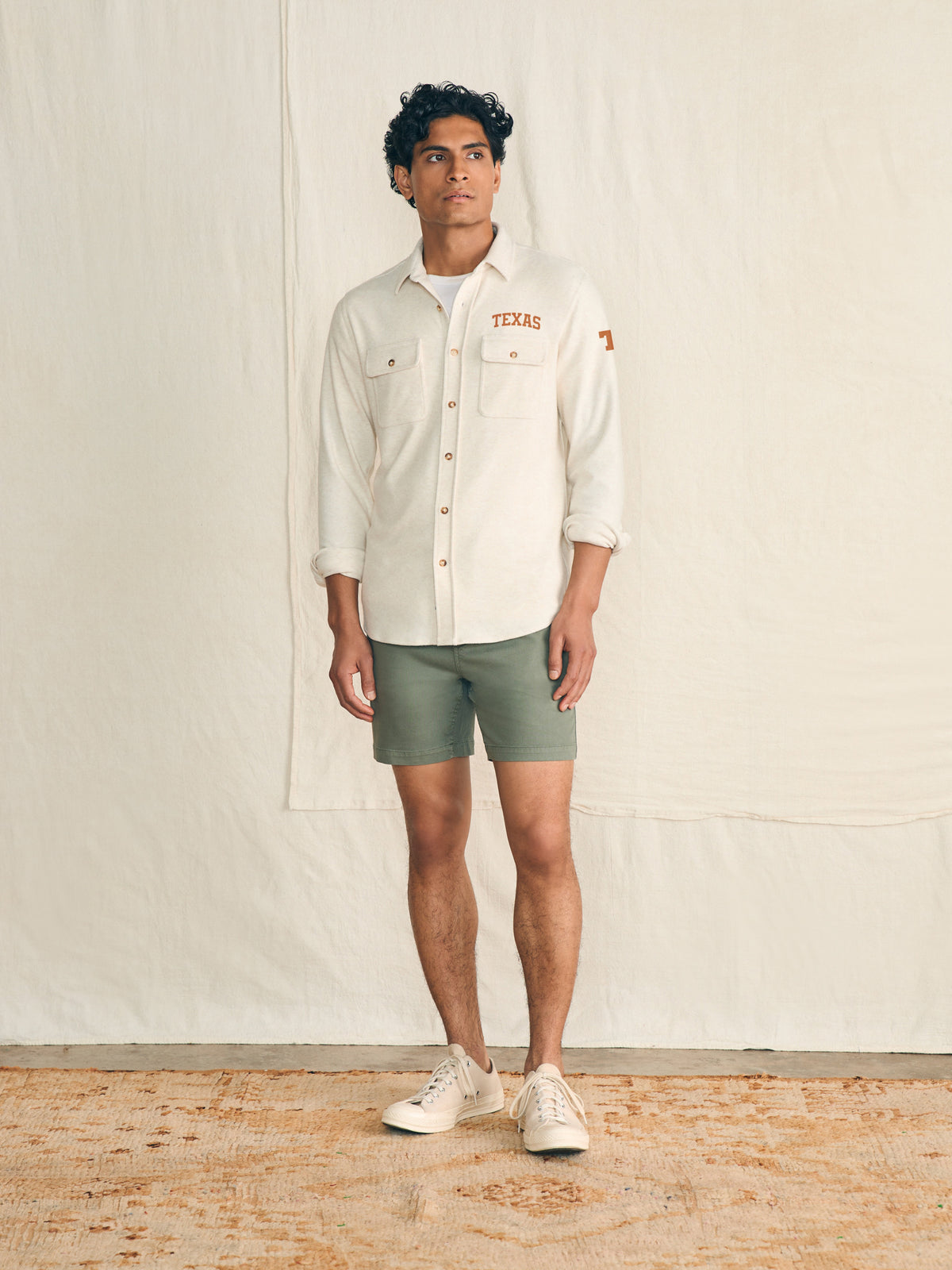 Man wearing a white shirt with UT Austin graphic on the left chest and shoulder against a beige background, image 3 of 3