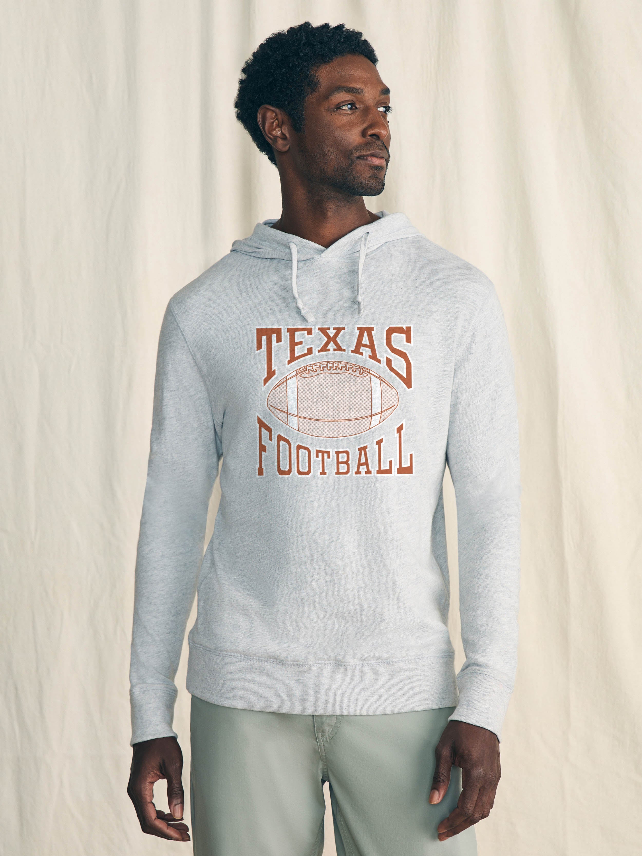 Man is wearing a light grey hoodie with UT Austin graphic on the center front against a beige background