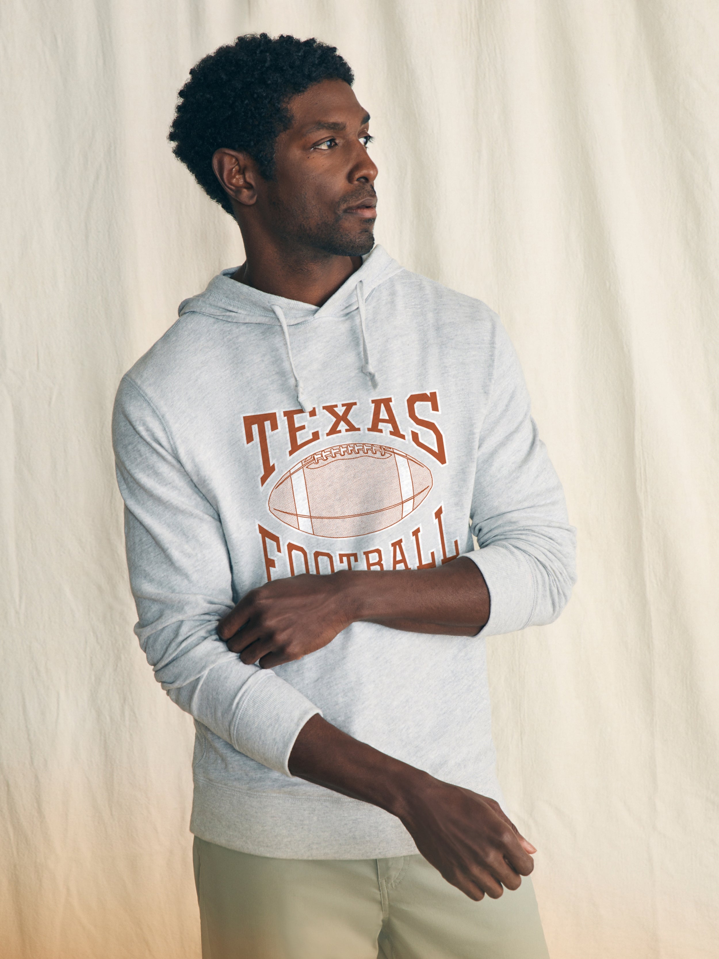 Man is wearing a light grey hoodie with UT Austin graphic on the center front against a beige background