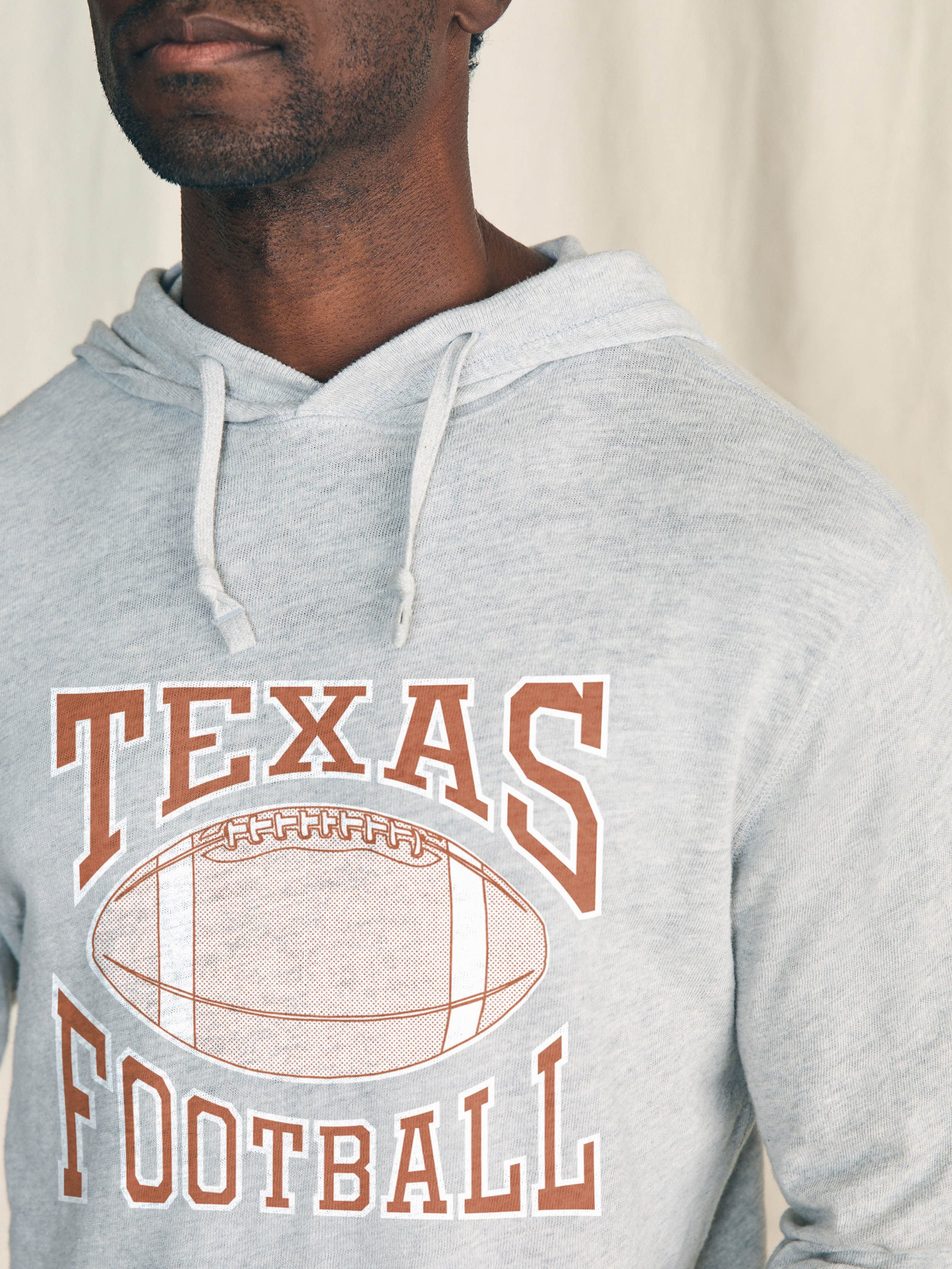 Man is wearing a light grey hoodie with UT Austin graphic on the center front against a beige background