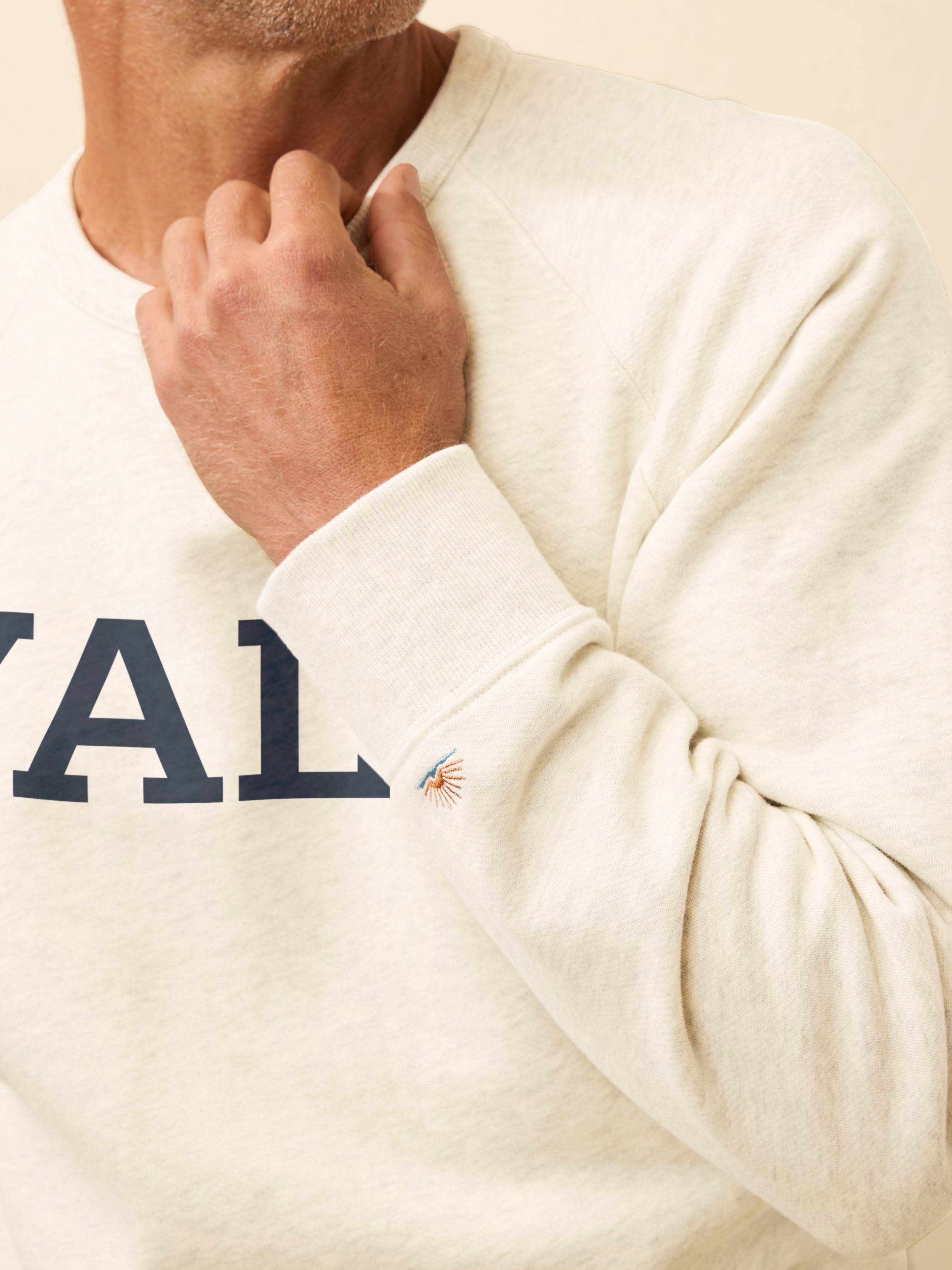 Man wearing a white sweatshirt with Yale graphic printed on it against a beige background