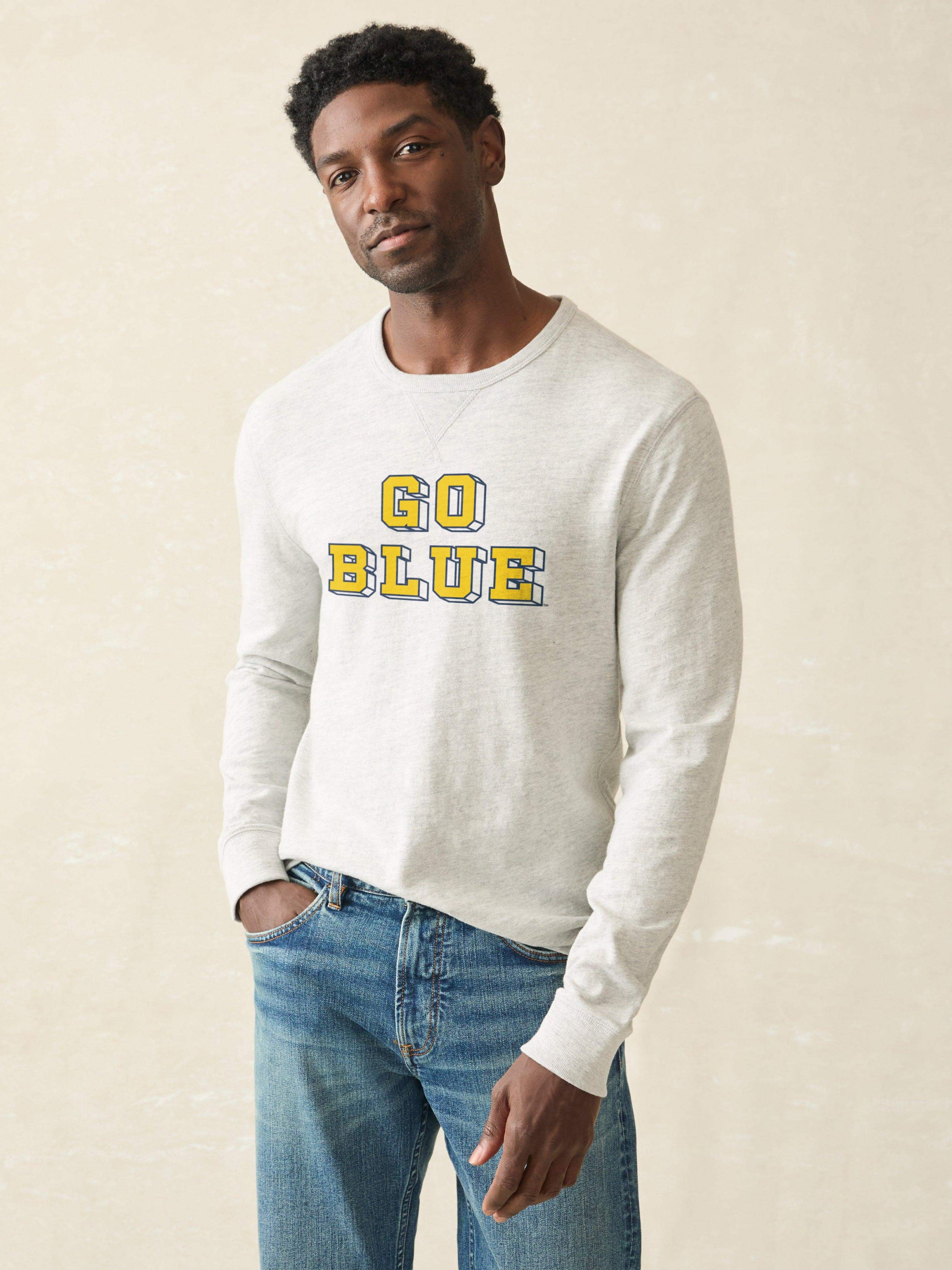 Man wearing a grey sweatshirt with Michigan graphic on the front against a beige background