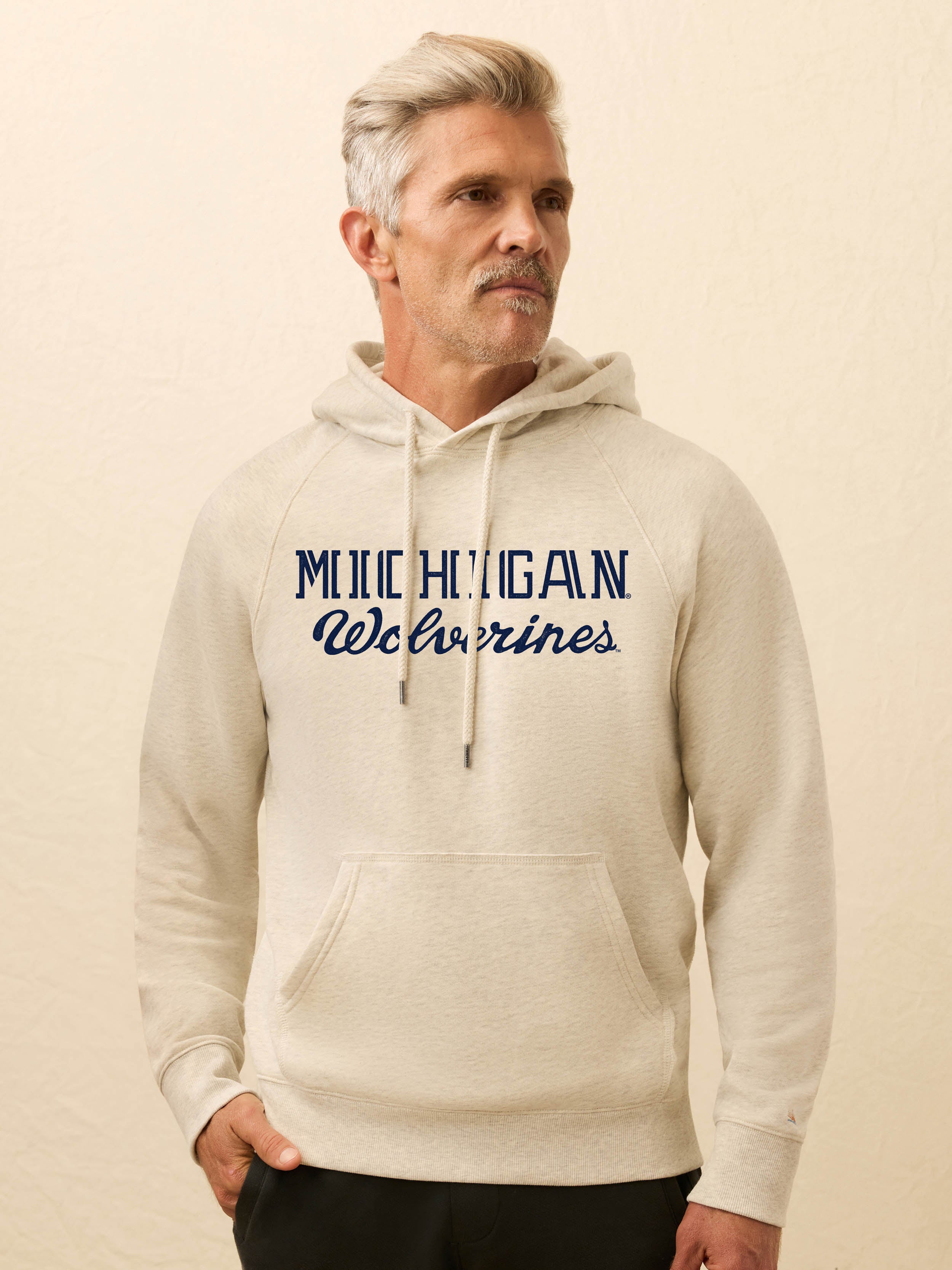 Man wearing a beige hoodie with 'Michigan Wolverines' text on a beige background
