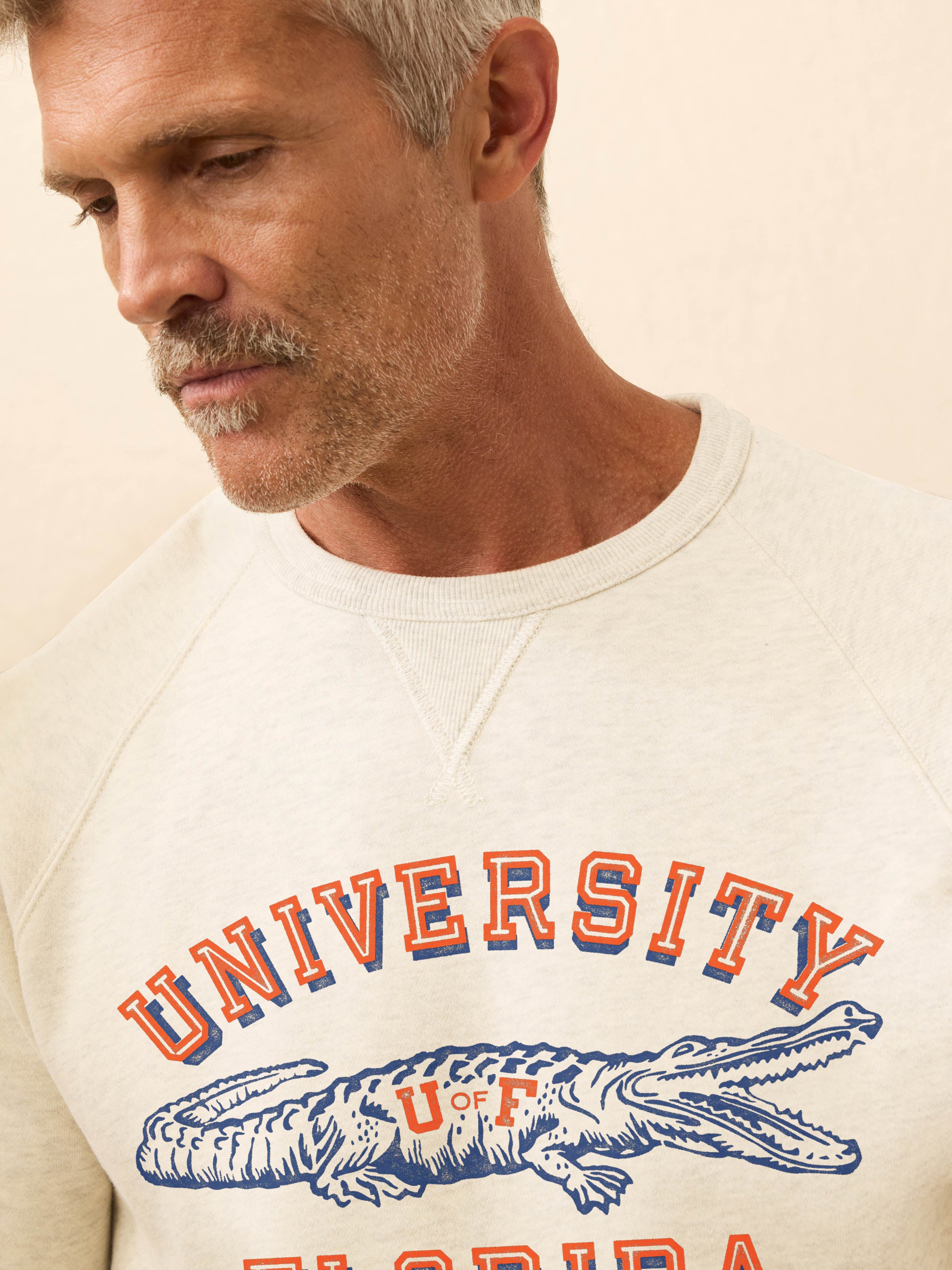 Man wearing a white crewneck sweatshirt with Florida graphic on the chest against a beige background