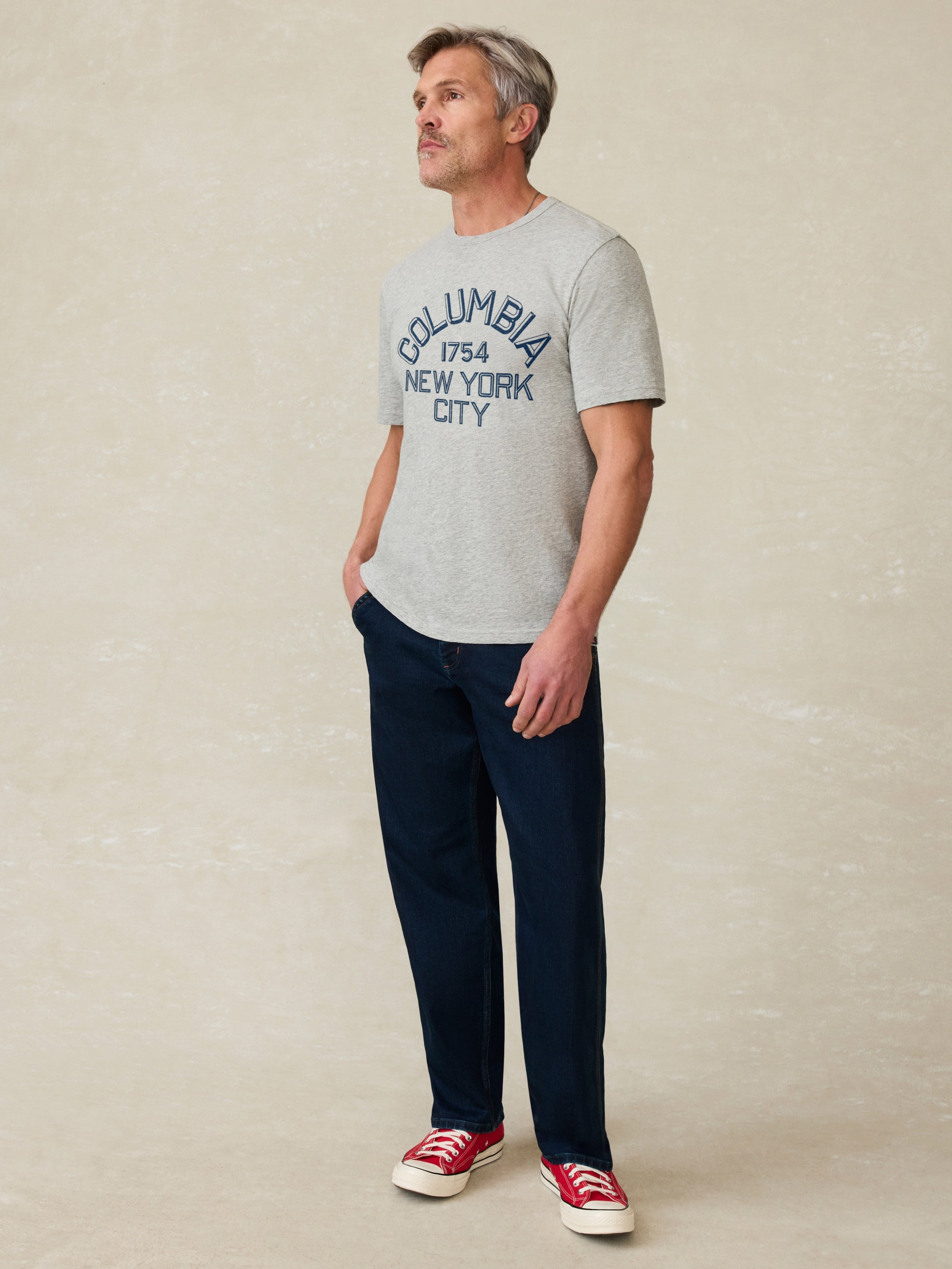 Man wearing a grey short sleeve t-shirt with Columbia graphic on the center front against a beige background