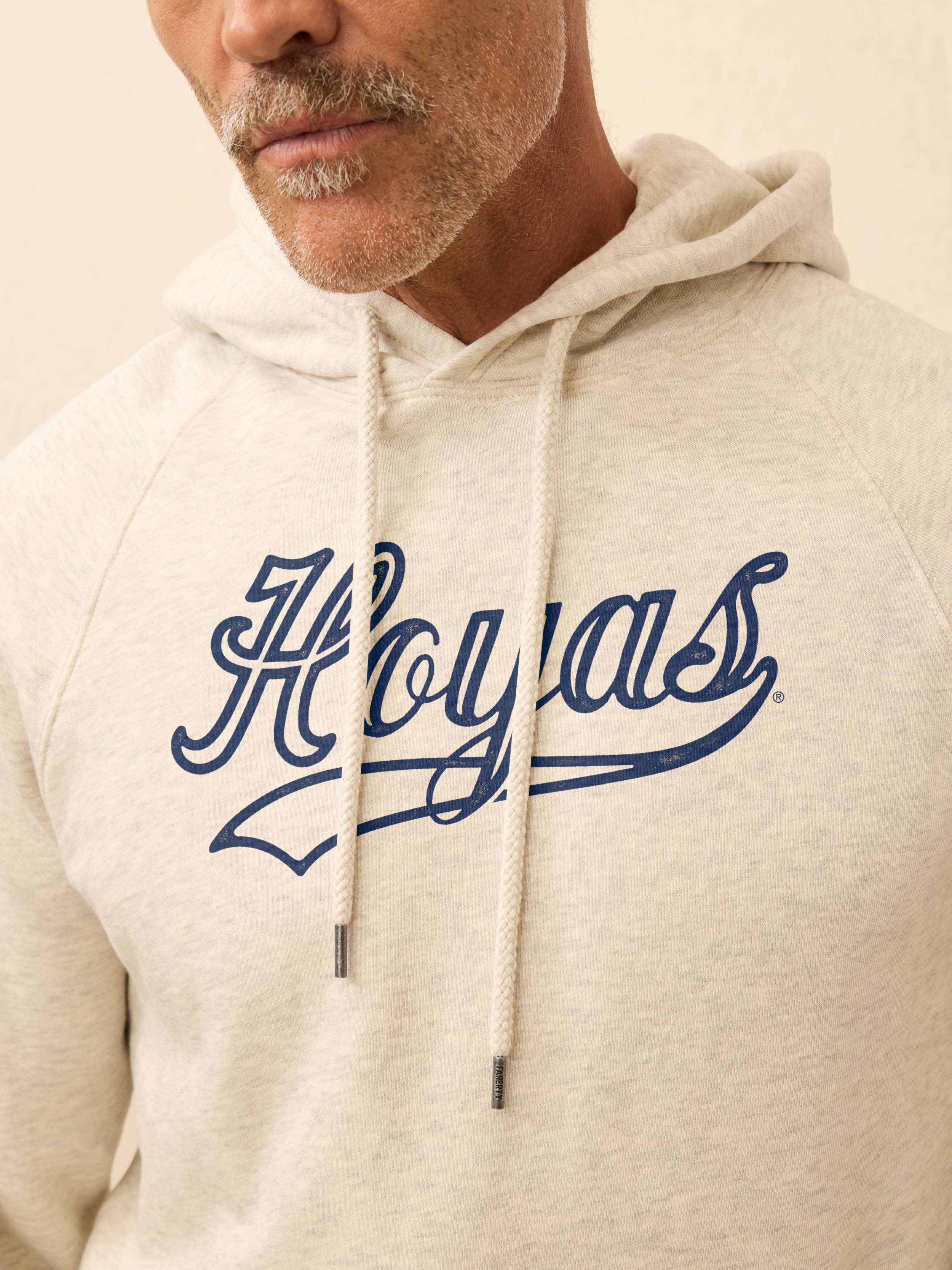 Man wearing an ivory heather hoodie with Georgetown graphic on the center chest against a beige background