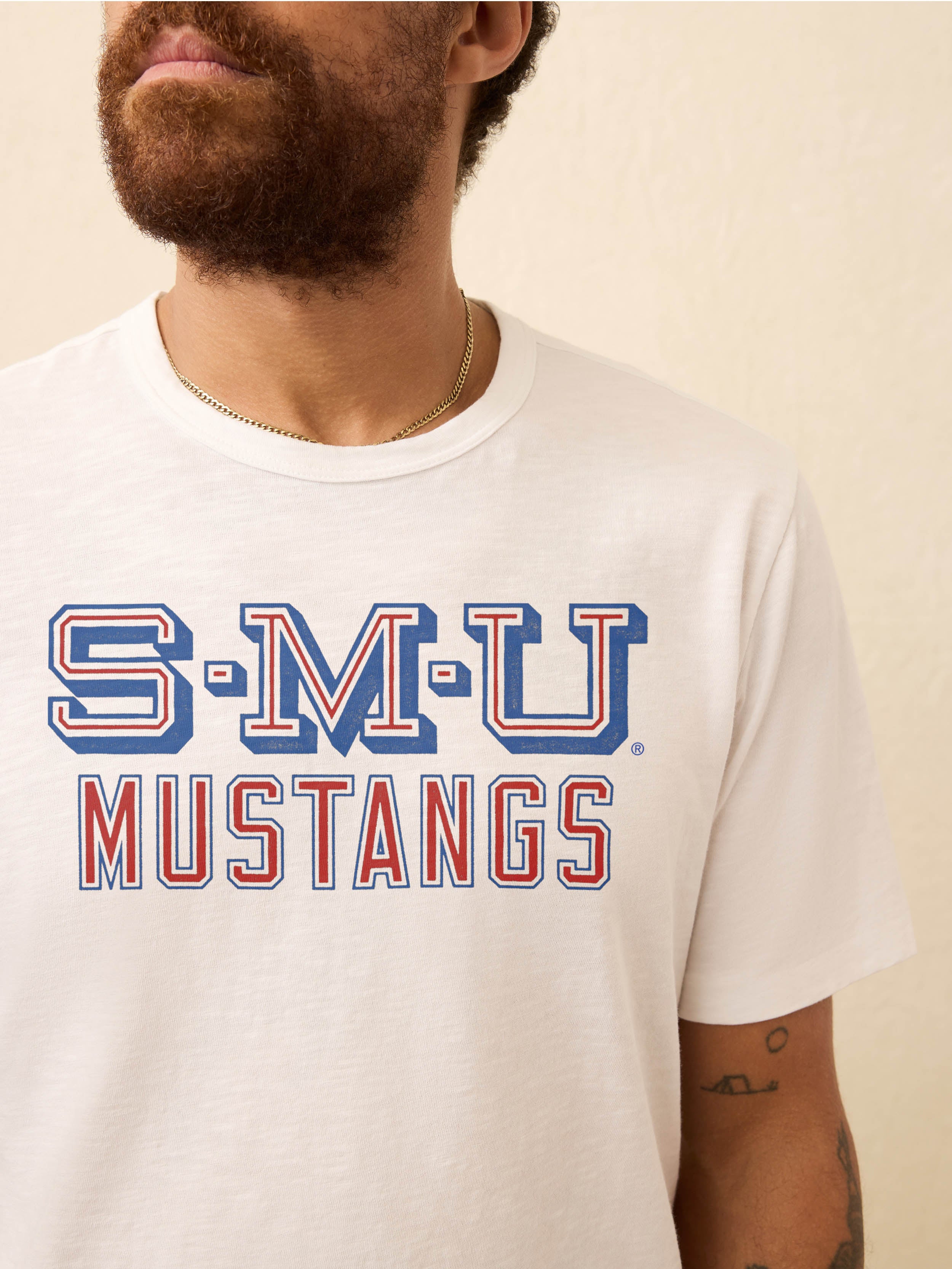 Man wearing a white t-shirt with SMU graphic on the front against a beige background