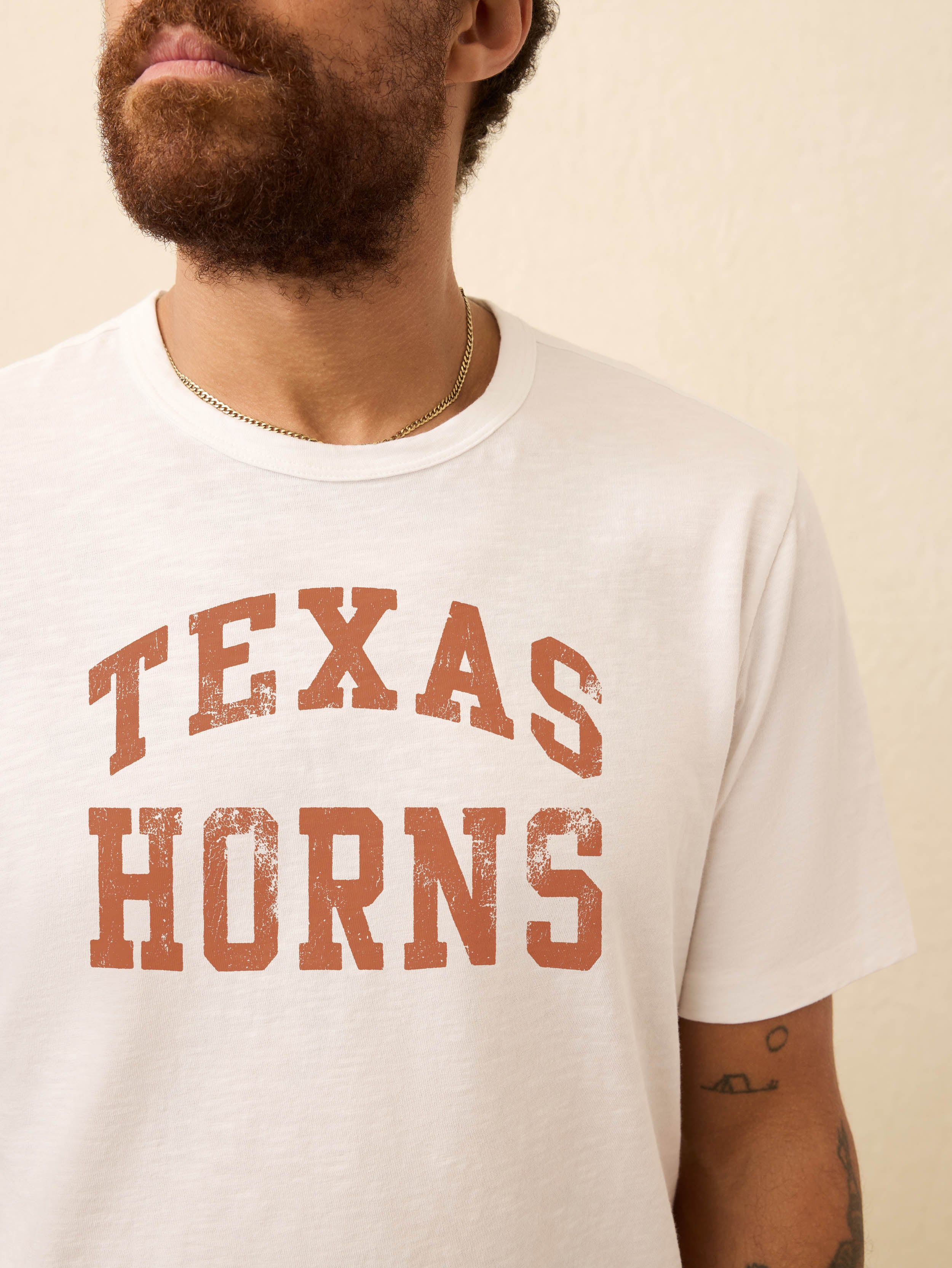Man wearing a white short sleeve t-shirt with UT Austin graphic at the center front against a beige background