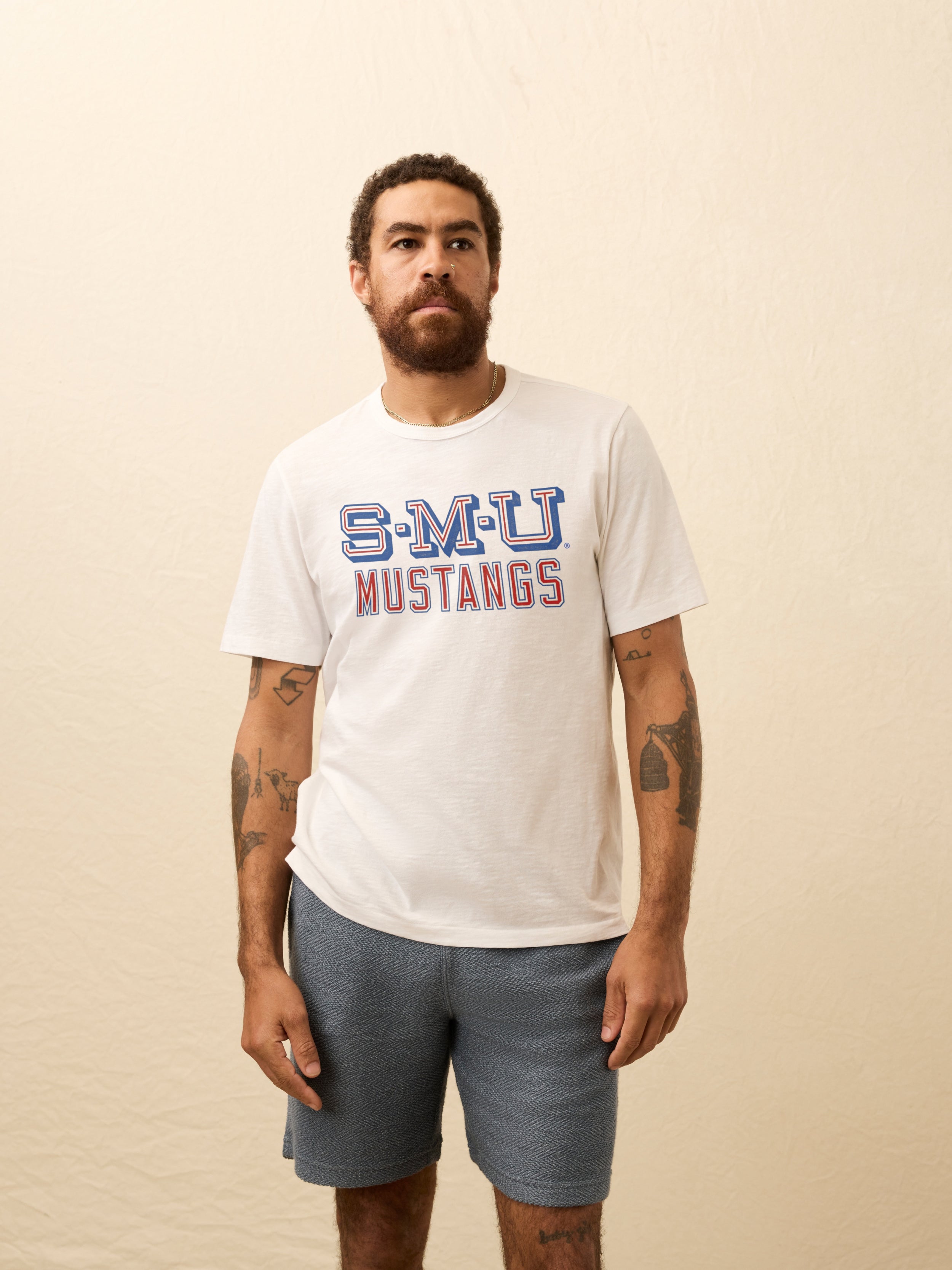Man wearing a white t-shirt with SMU graphic on the front against a beige background