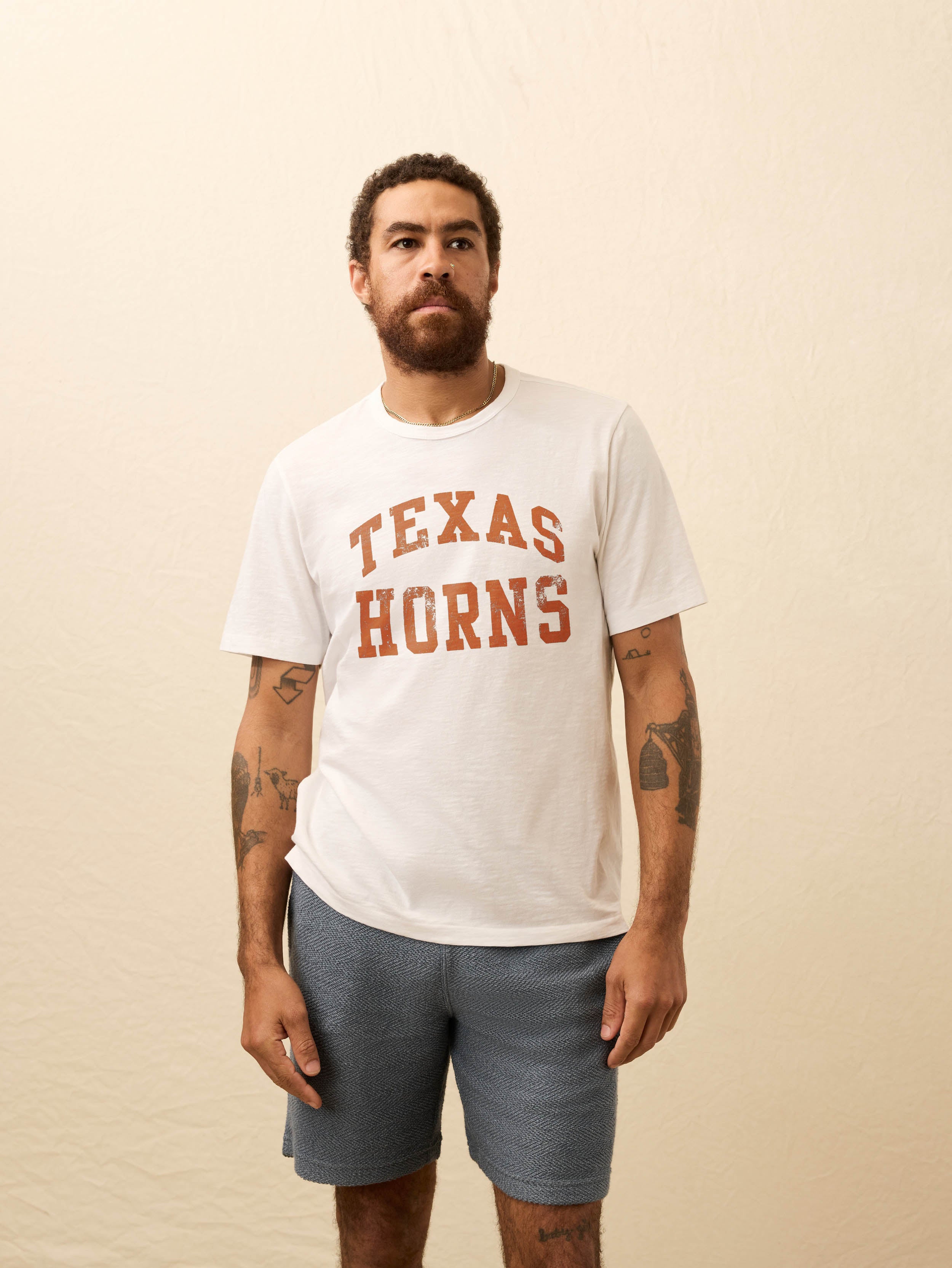 Man wearing a white short sleeve t-shirt with UT Austin graphic at the center front against a beige background