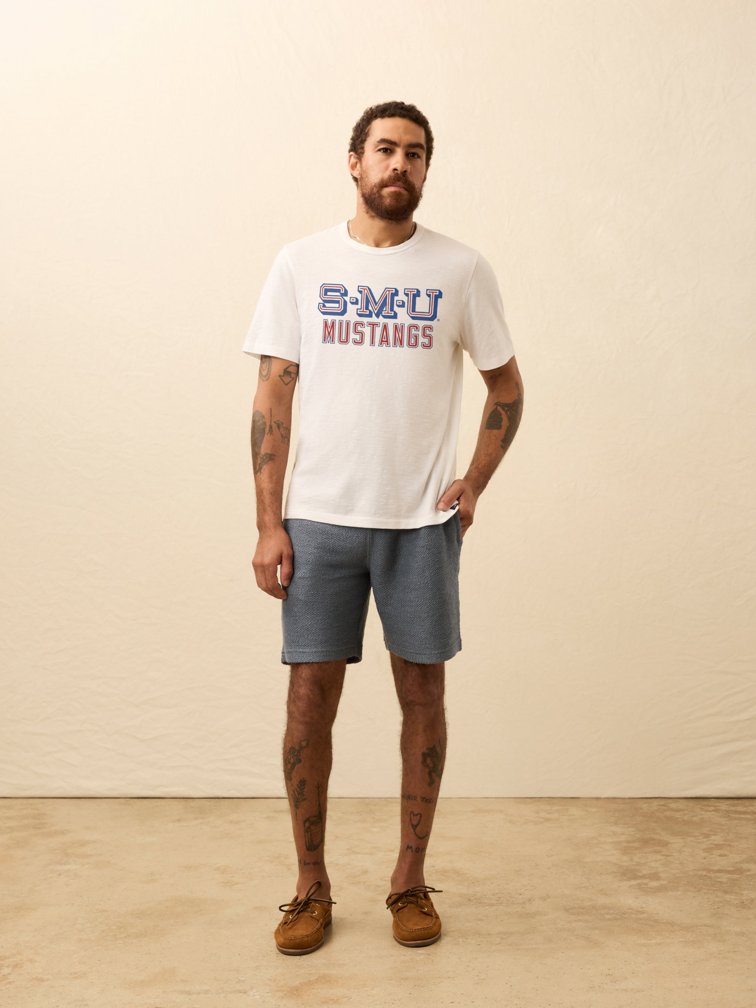 Man wearing a white t-shirt with SMU graphic on the front against a beige background