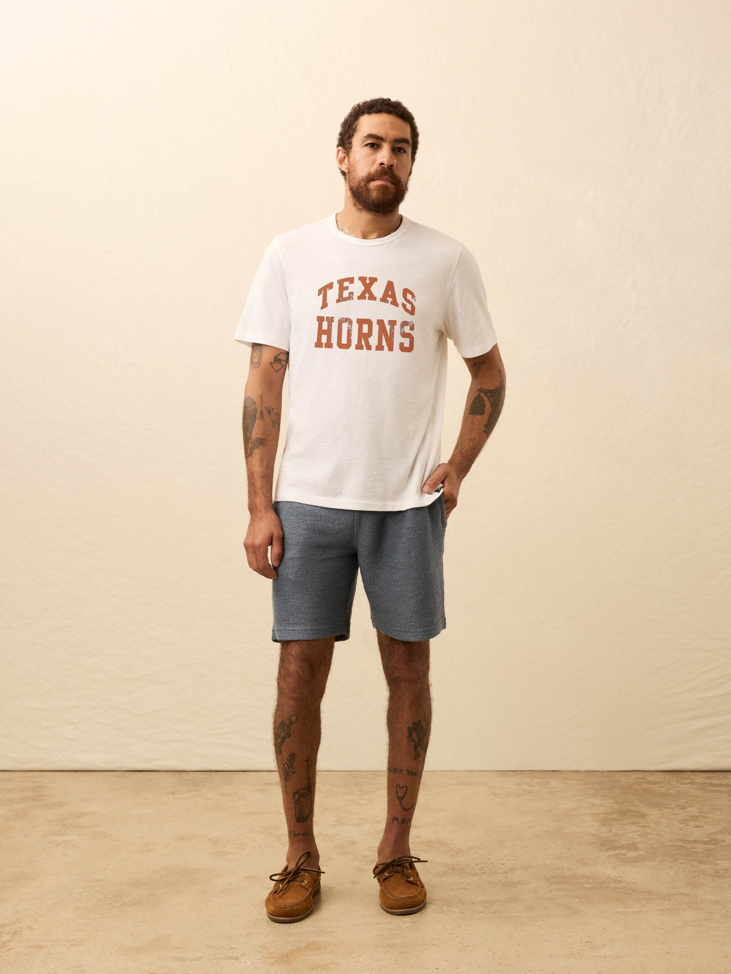 Man wearing a white short sleeve t-shirt with UT Austin graphic at the center front against a beige background