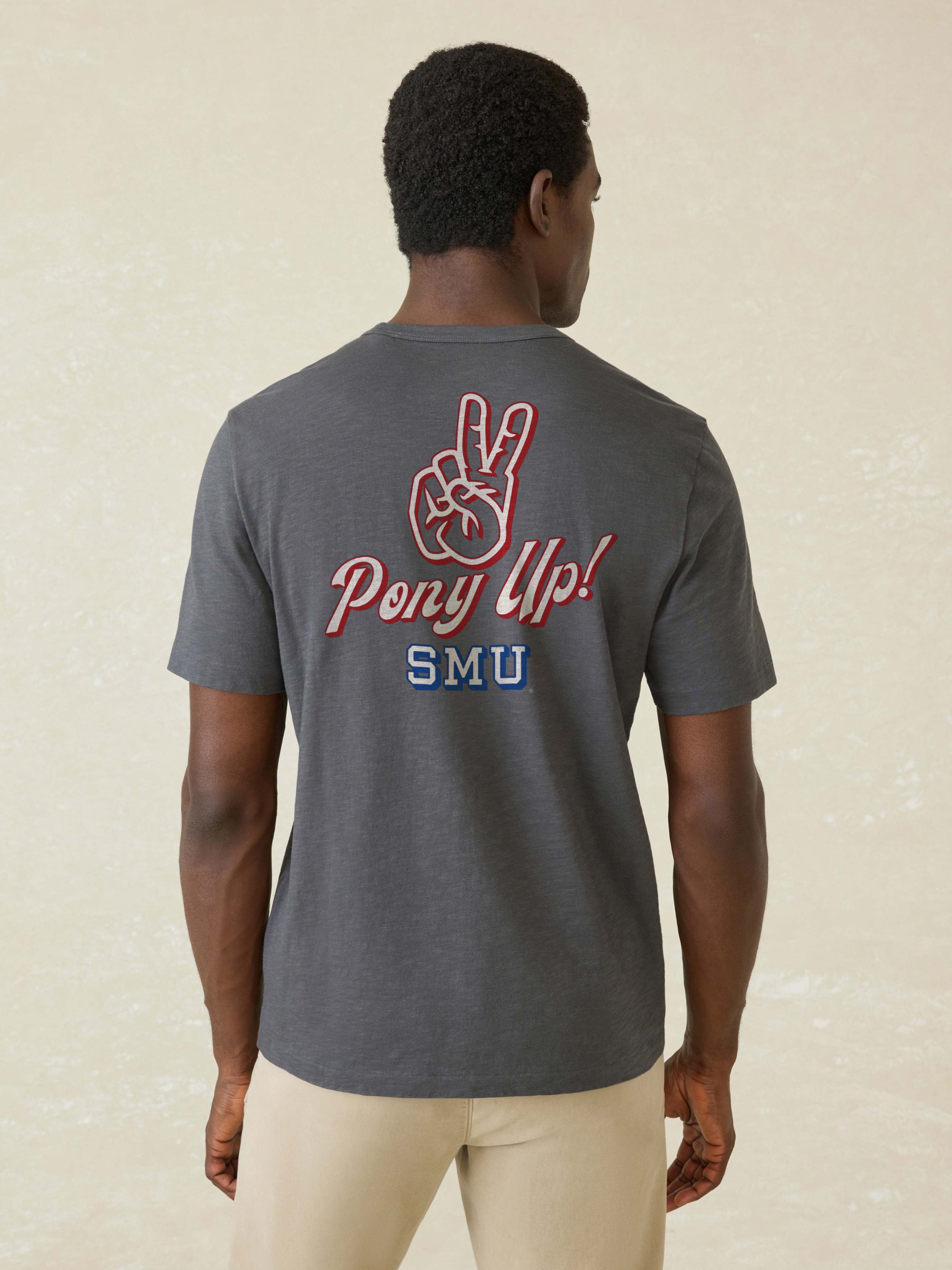 Man wearing a dark grey short sleeve t-shirt with SMU graphic on the center back against a beige background