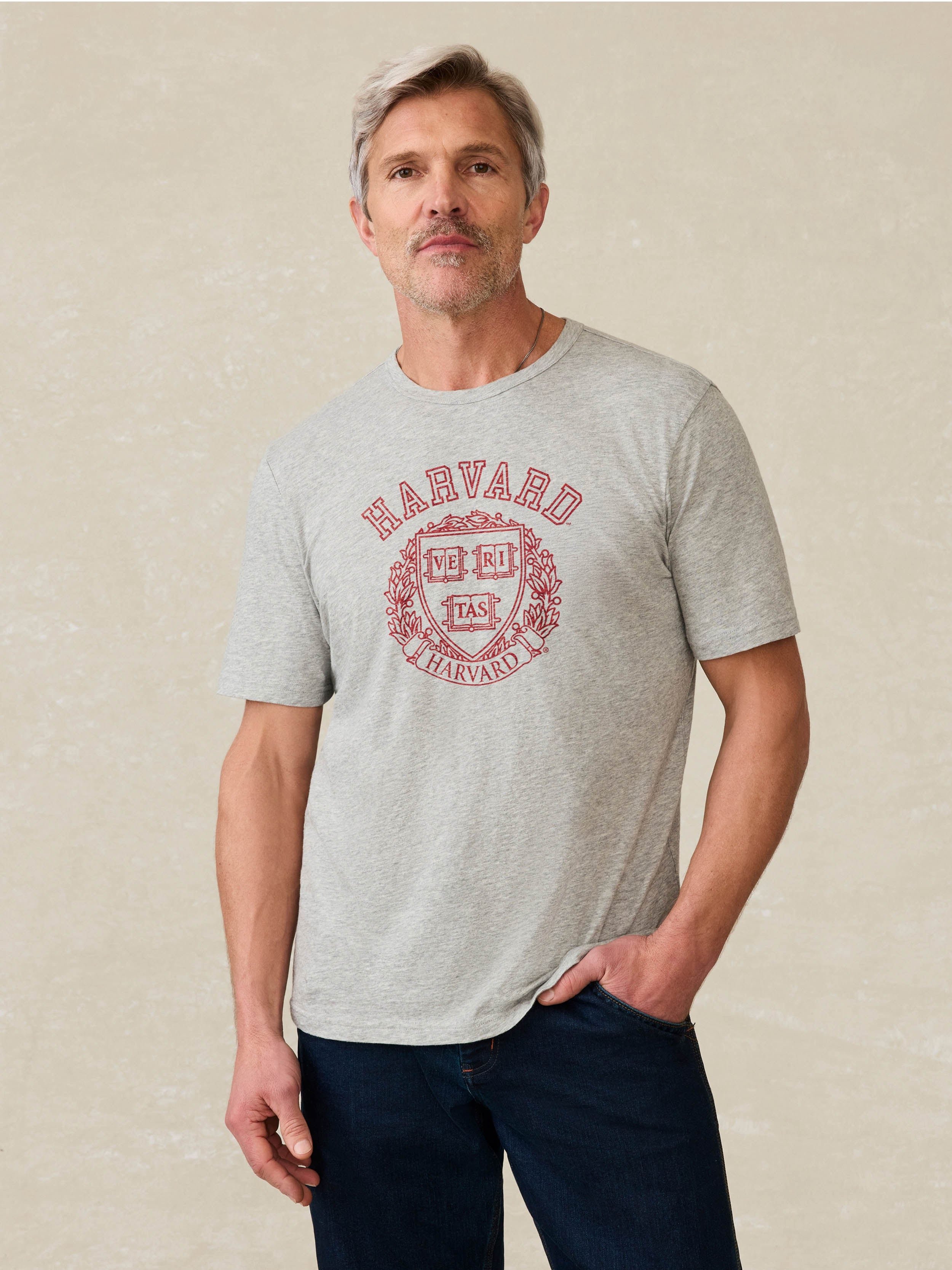 Man wearing a grey t shirt with Harvard graphic on the front against a beige background