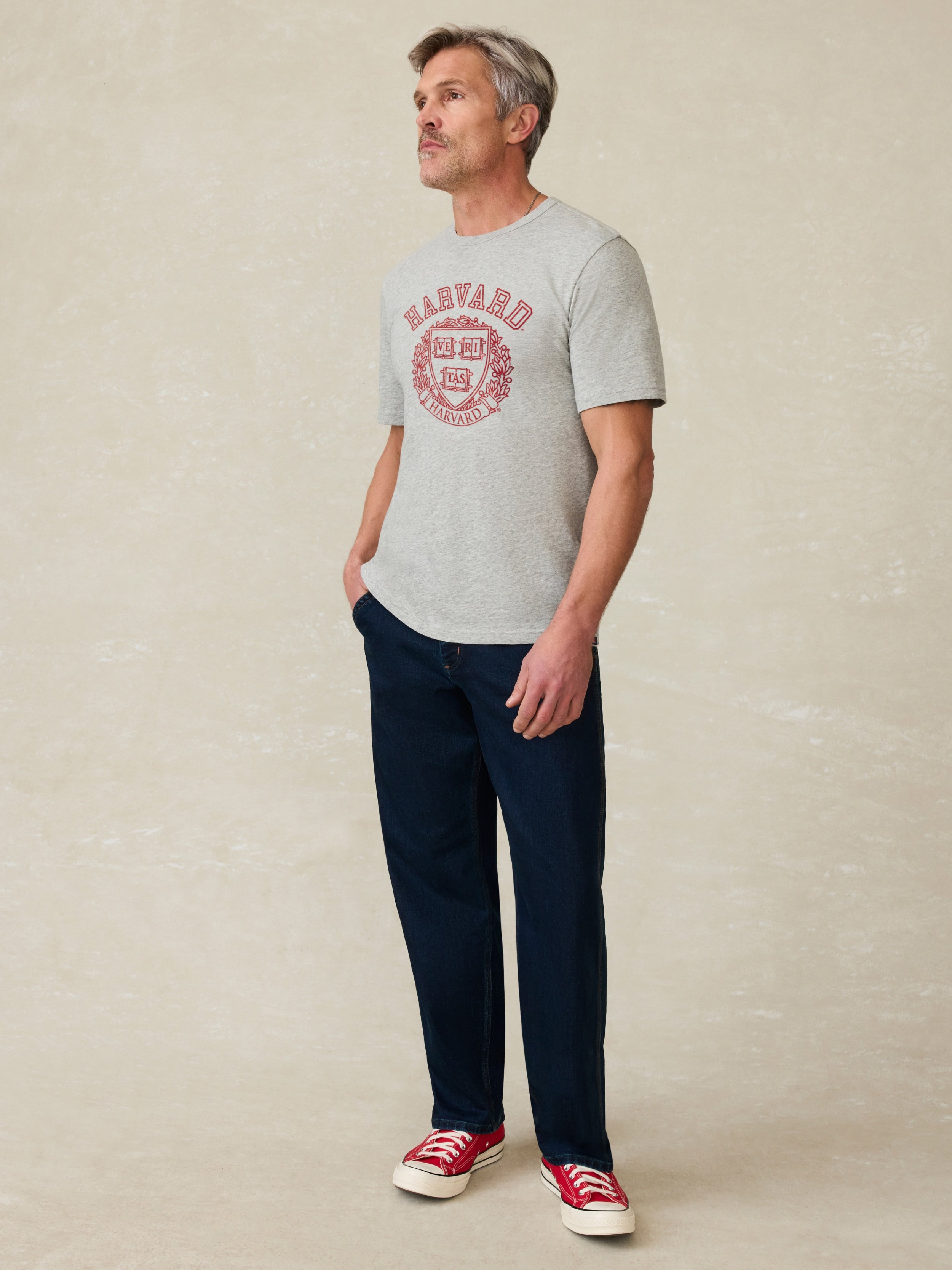 Man wearing a grey t shirt with Harvard graphic on the front against a beige background