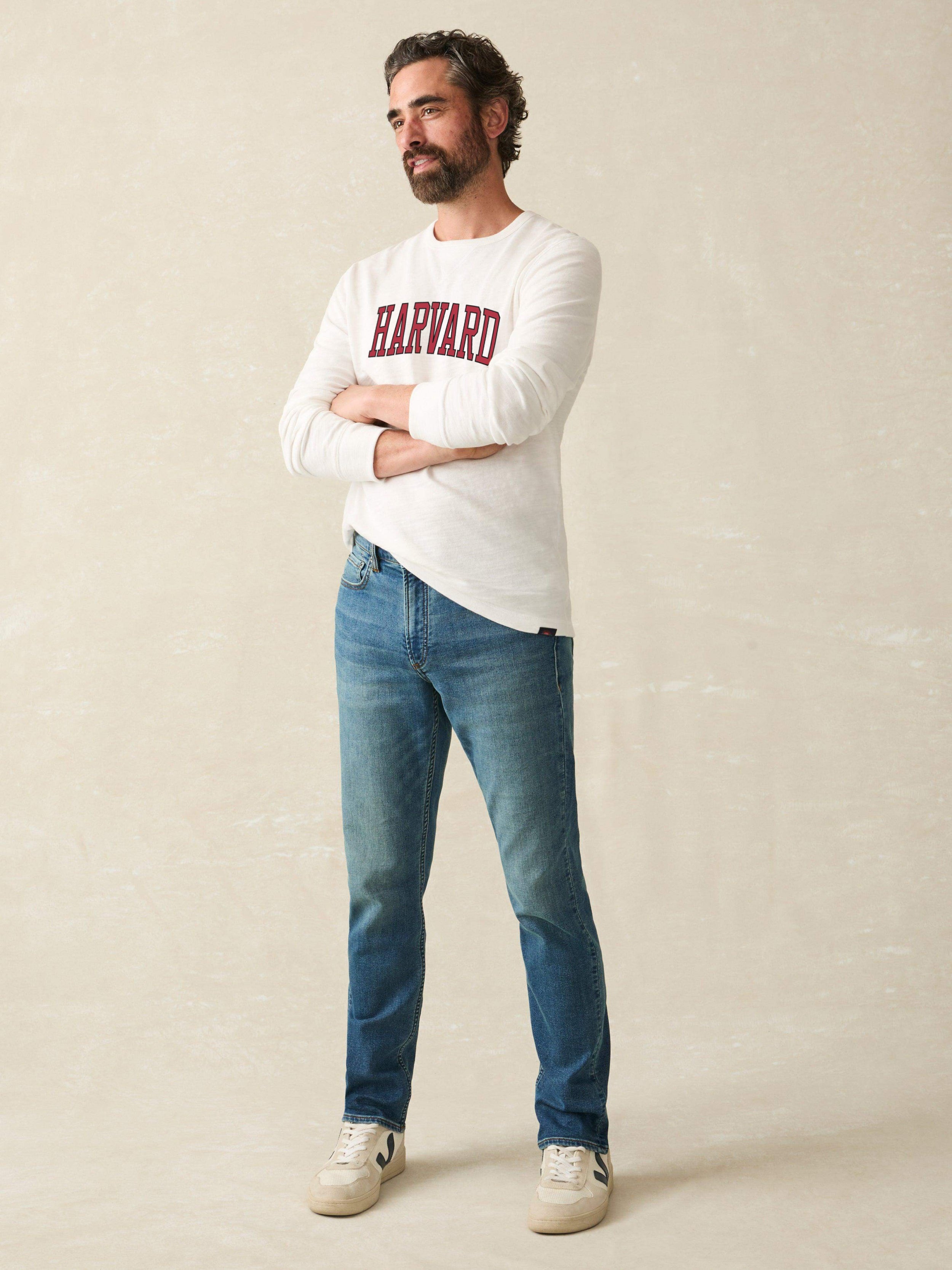 Man wearing a white long sleeve shirt with Harvard graphic at the center chest against a beige background