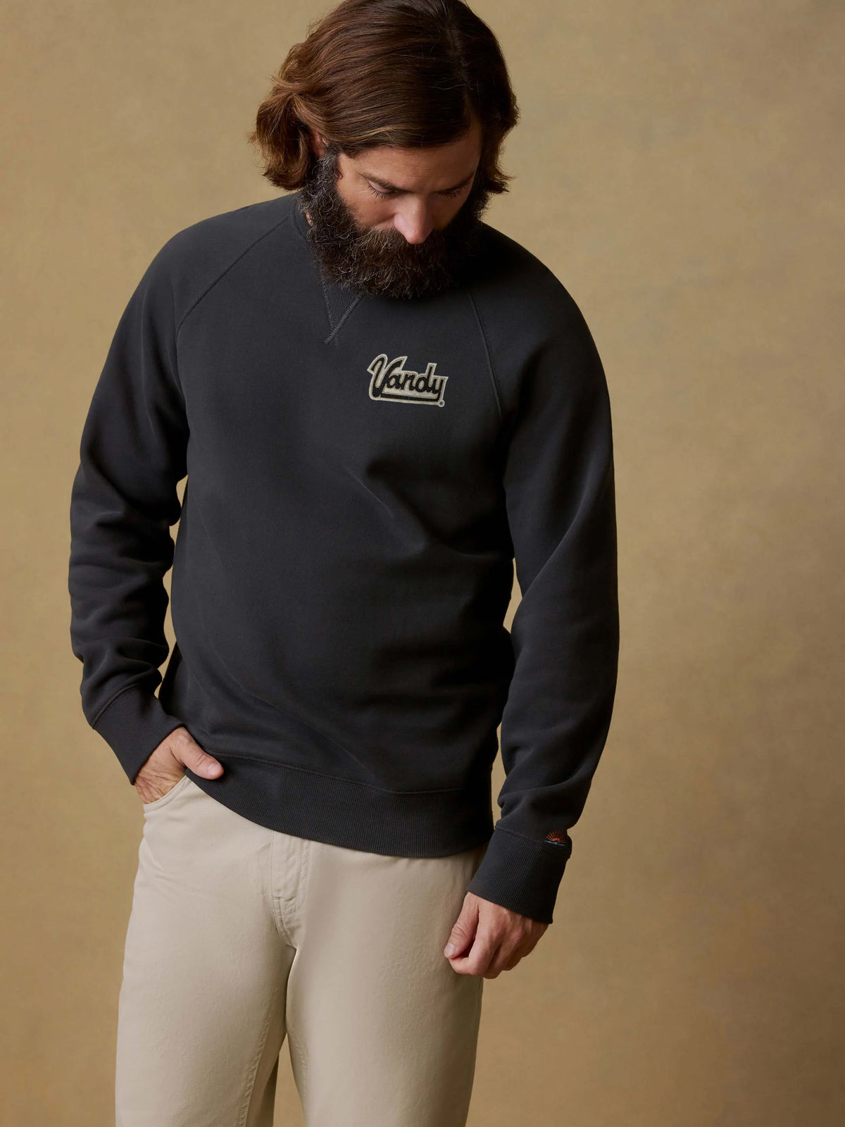 A man wearing a black Vanderbilt crewneck and beige pants, image 1 of 1