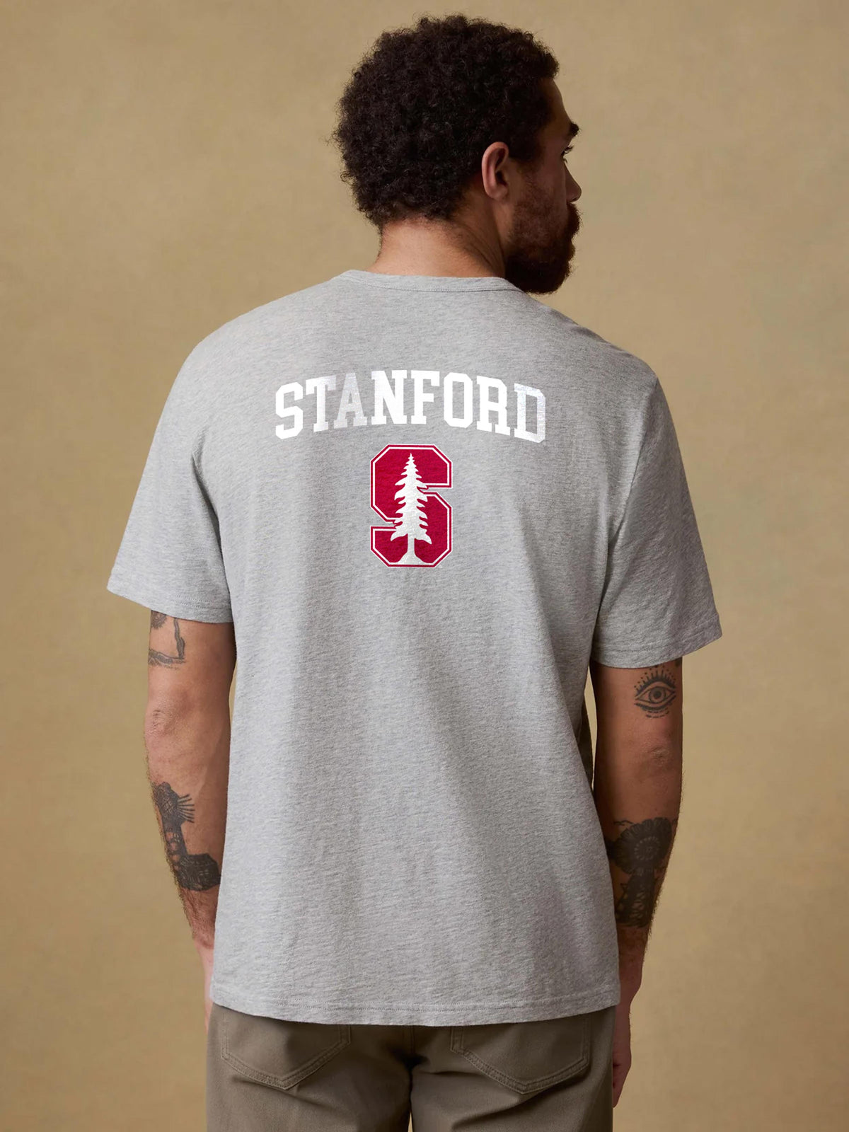 A man viewed from behind wearing a grey Stanford University tee and brown pants, image 2 of 2
