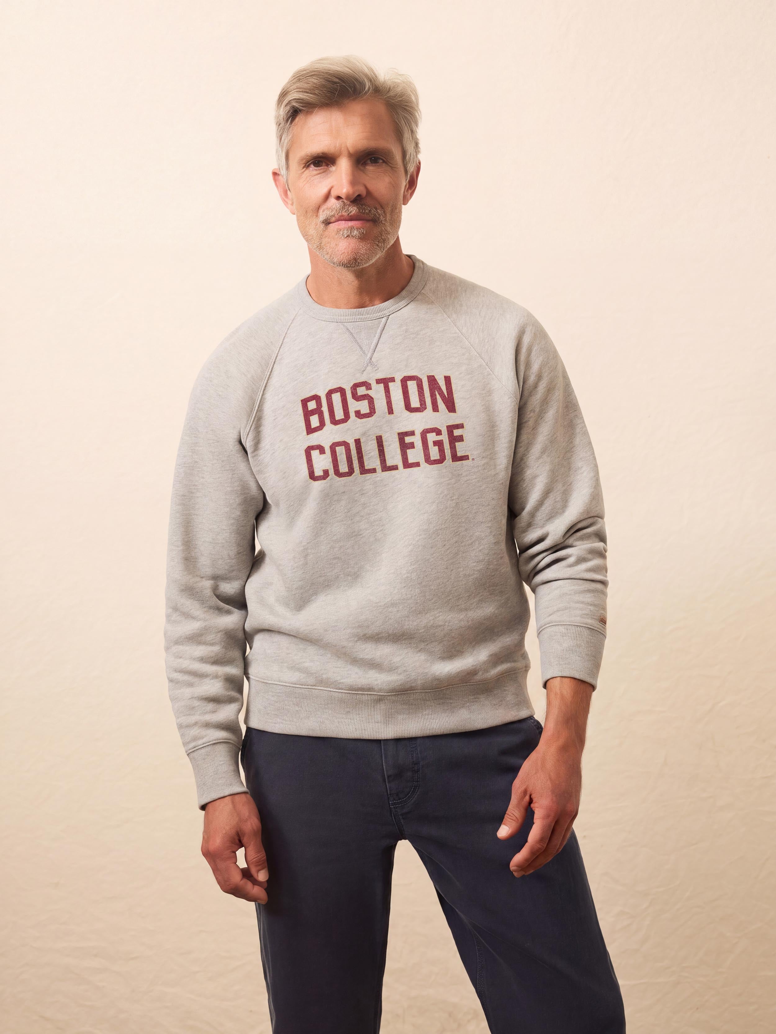 A man wearing a grey Boston College crewneck and blue pants
