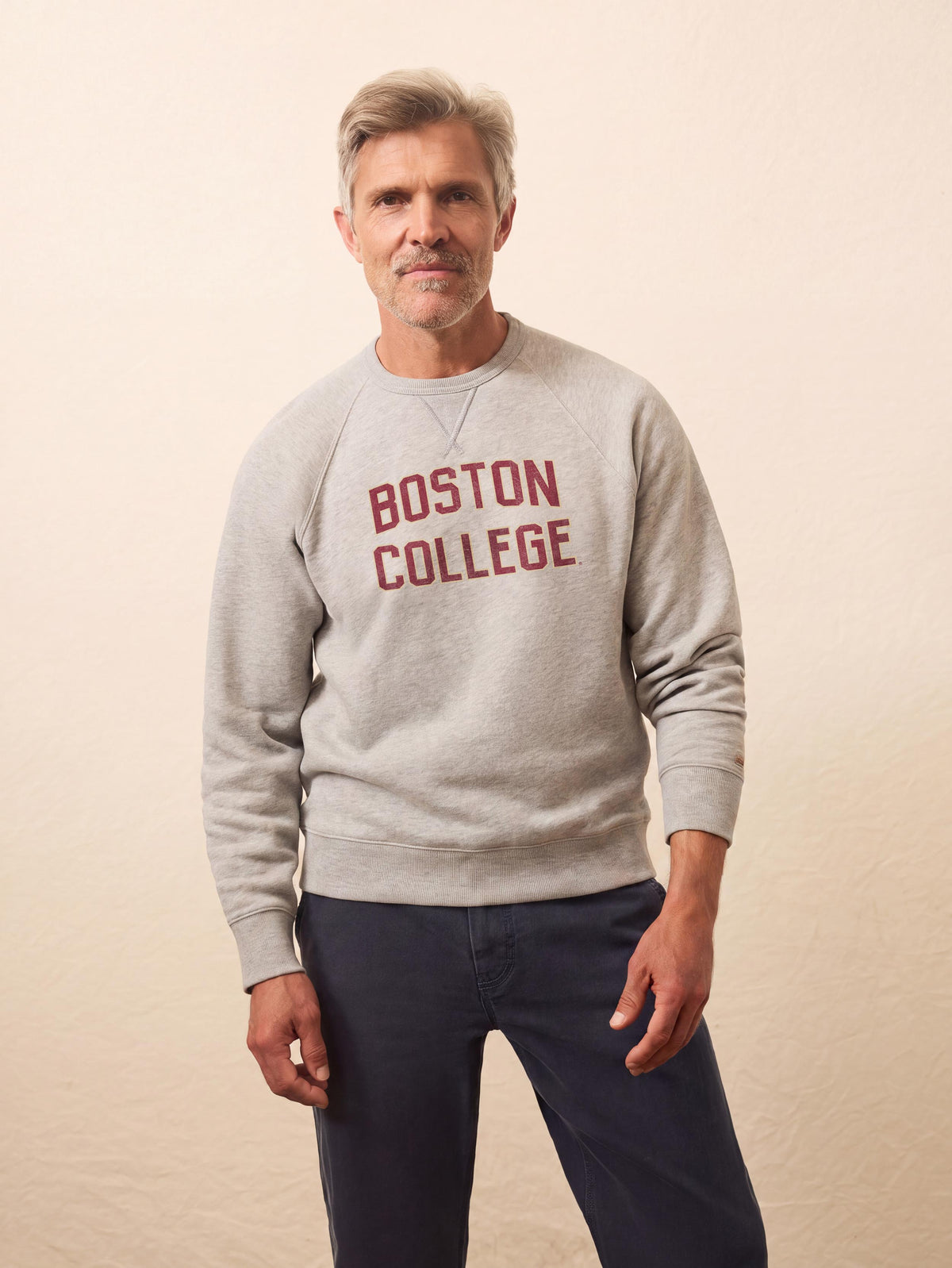 A man wearing a grey Boston College crewneck and blue pants, image 1 of 1