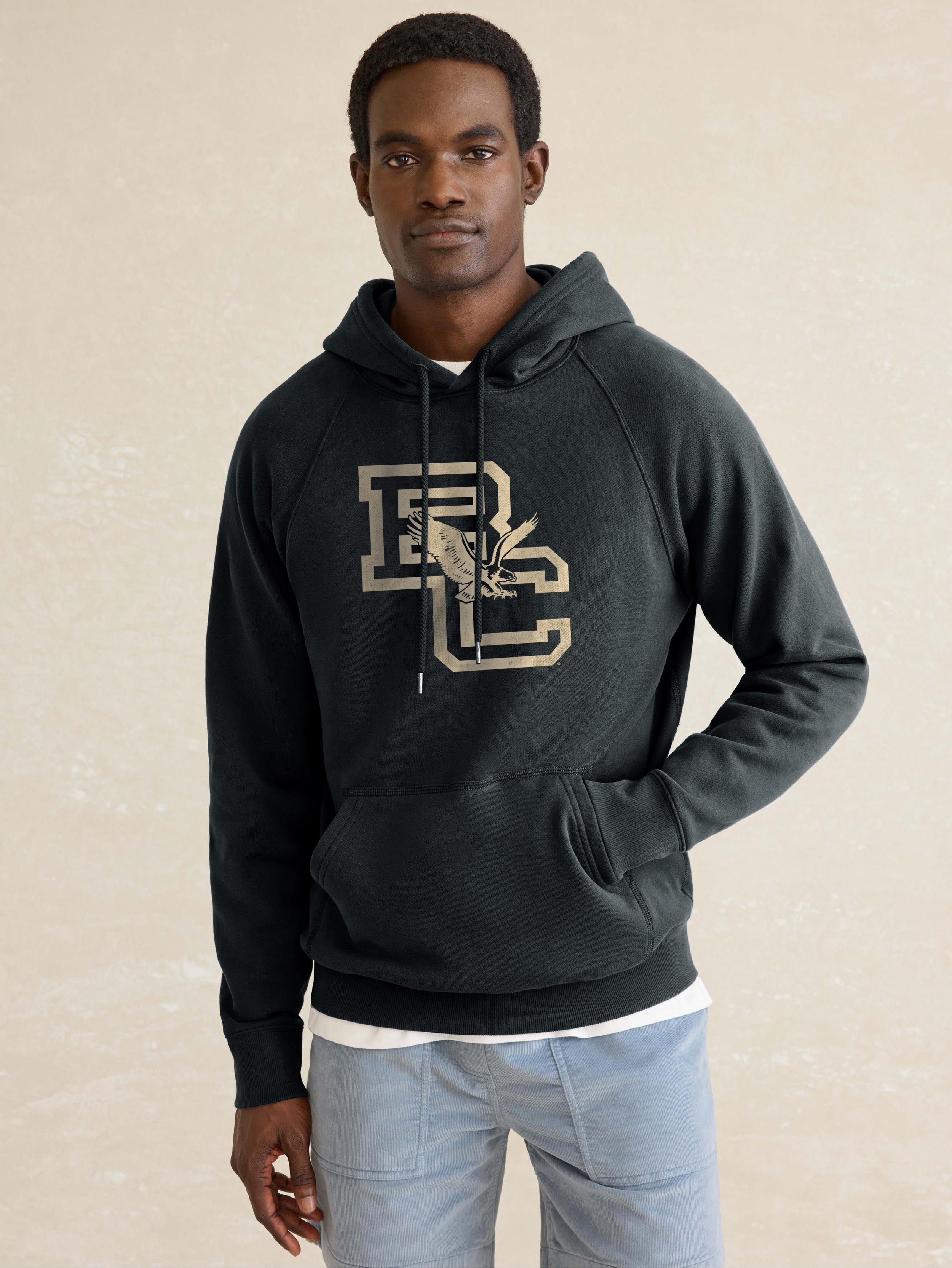 A man wearing a black Boston College hoodie and blue jeans