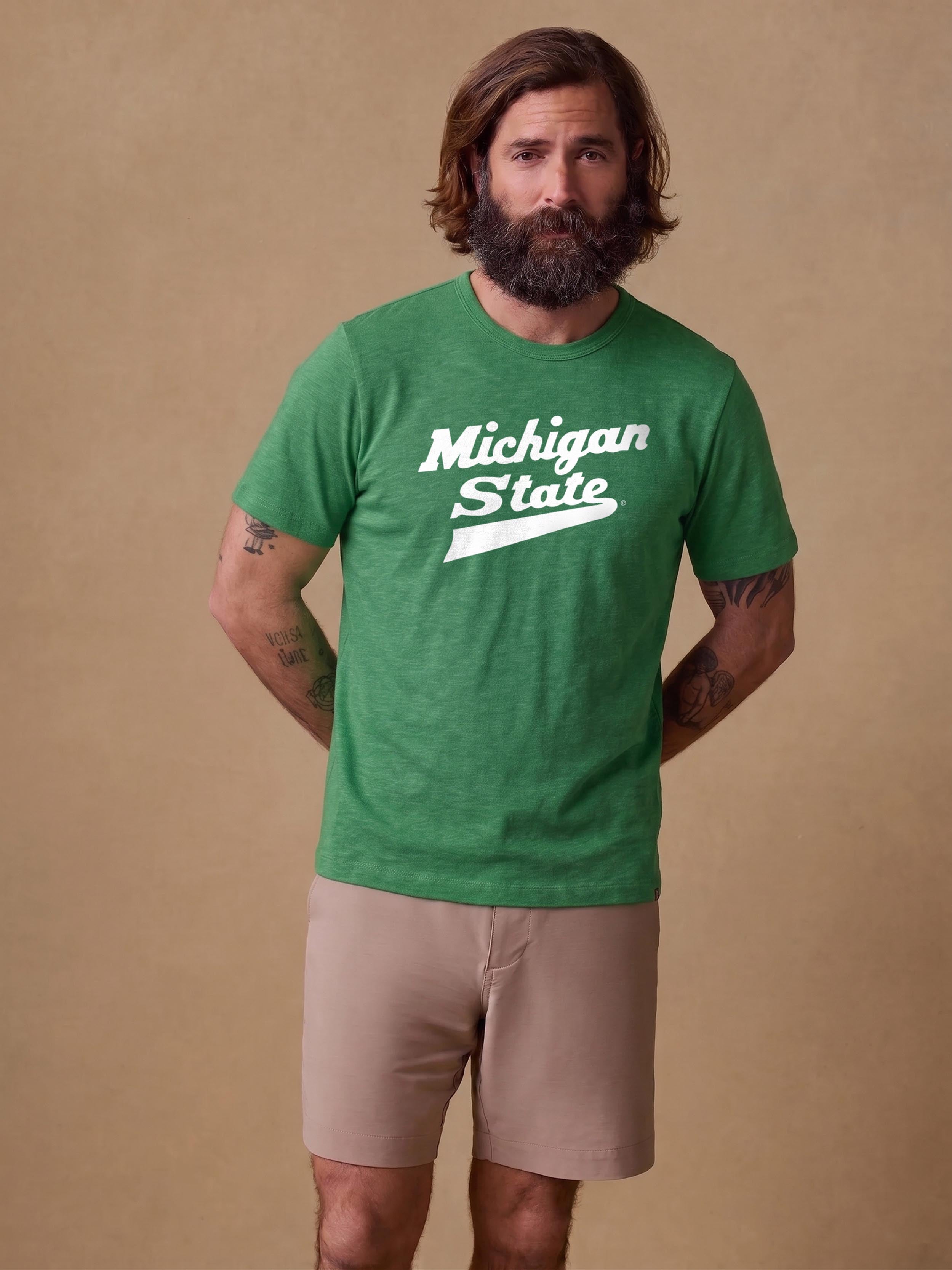 A man wearing a green Michigan State tee and beige shorts