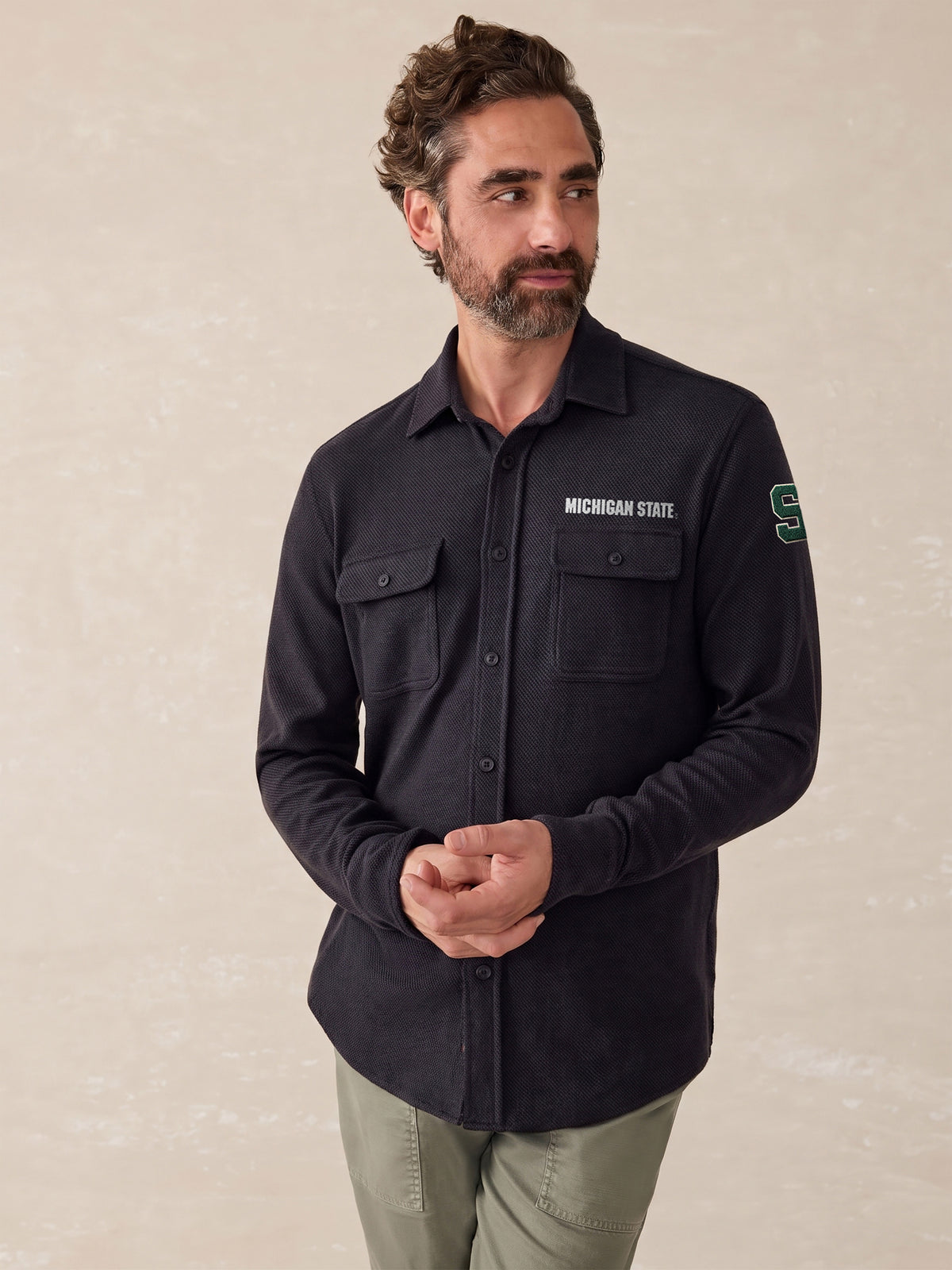 A man wearing a black Michigan State button up shirt and green pants, image 1 of 1