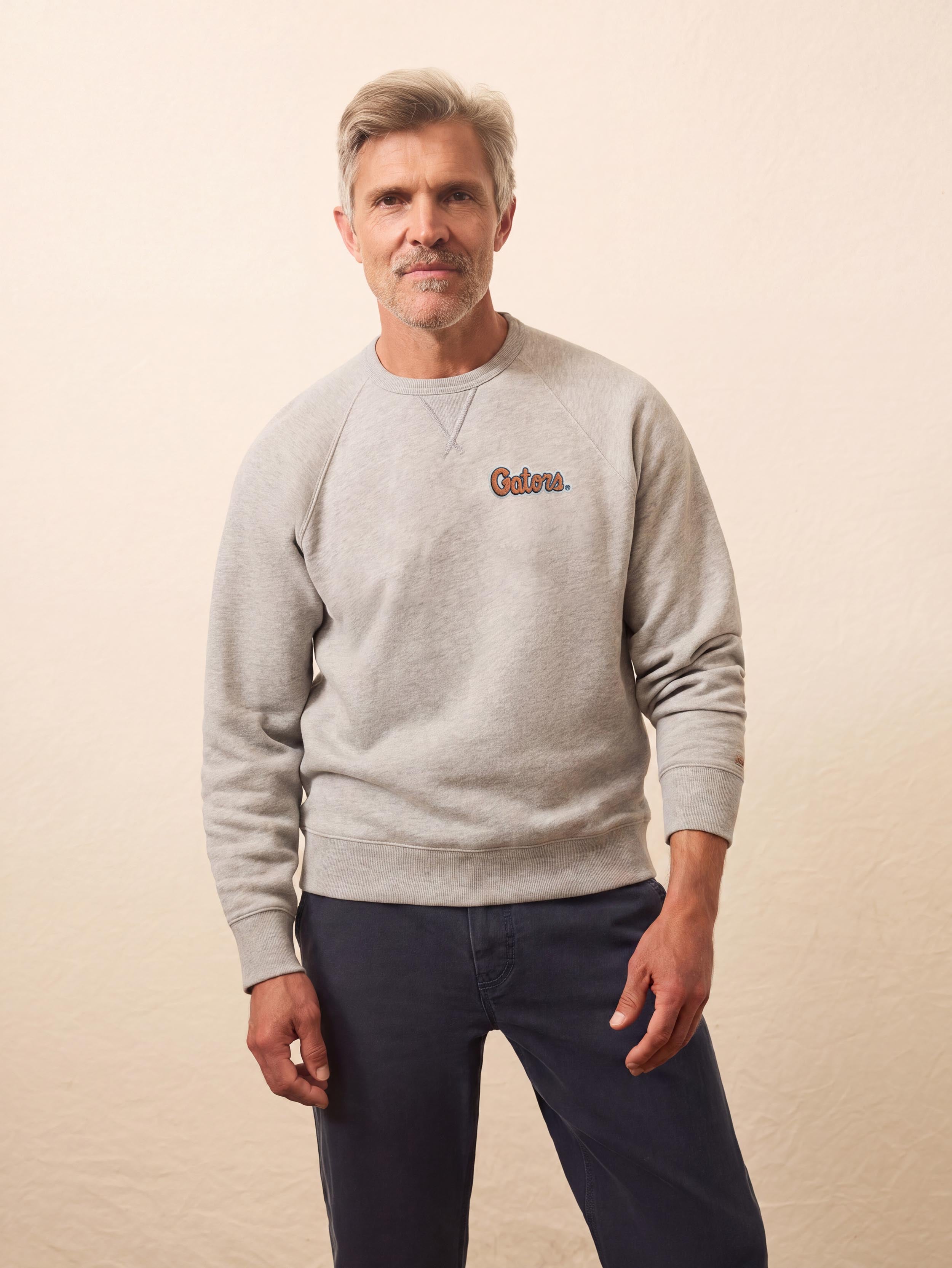 A man wearing a grey University of Florida crewneck and blue pants