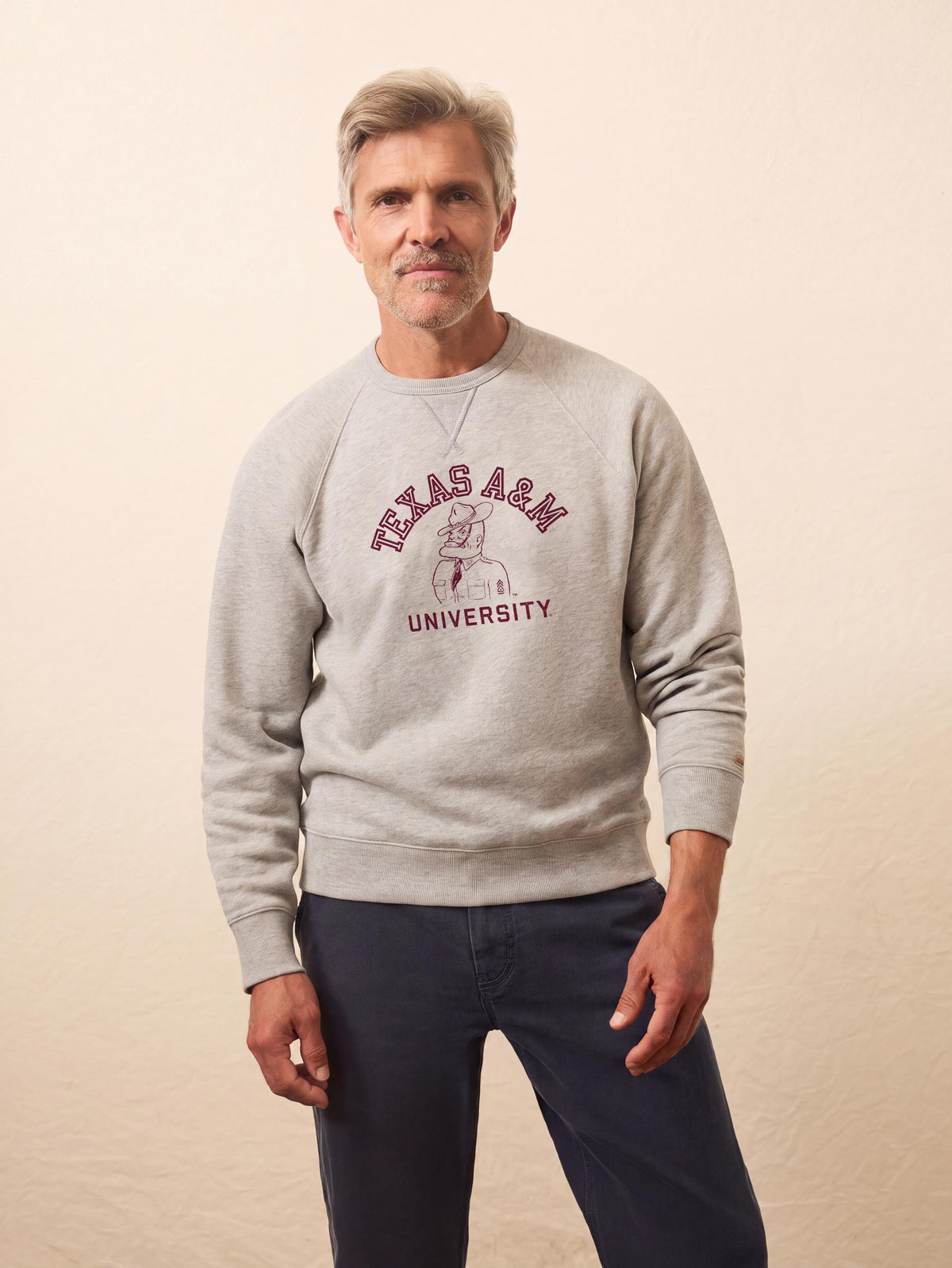 A man wearing a grey Texas A&M crewneck and blue pants, image 1 of 1