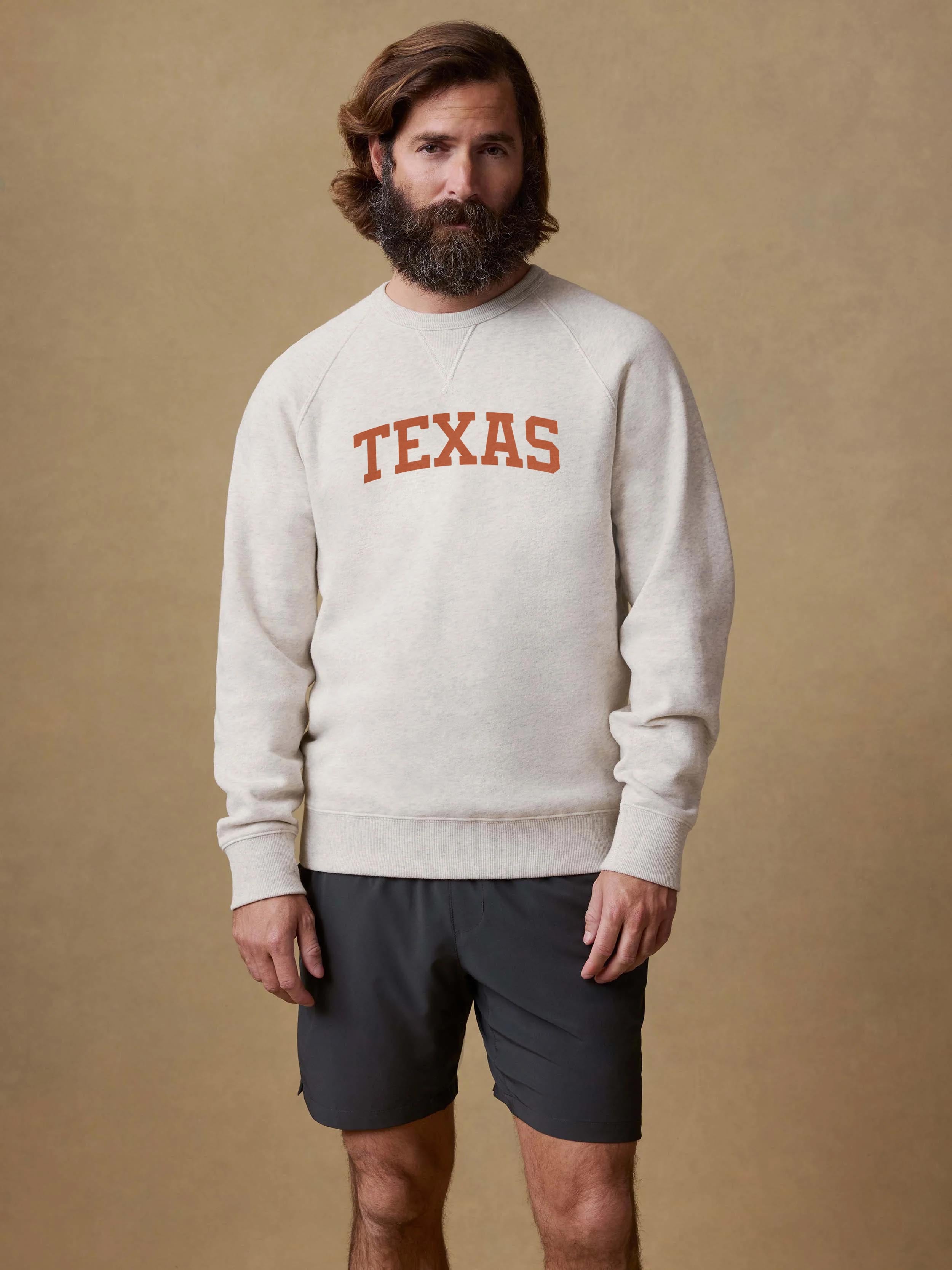 A man wearing a grey University of Texas crewneck and black shorts