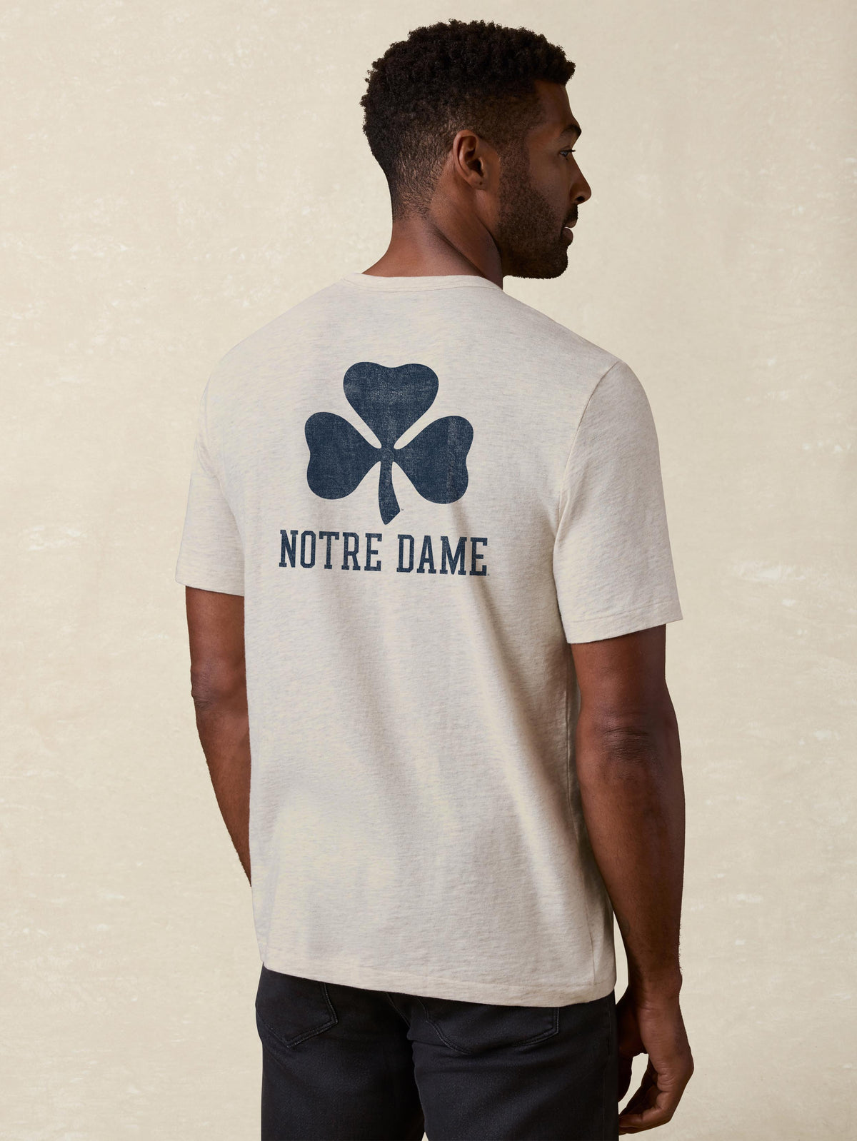 A man viewed from behind wearing a grey Notre Dame tee and black jeans, image 2 of 2
