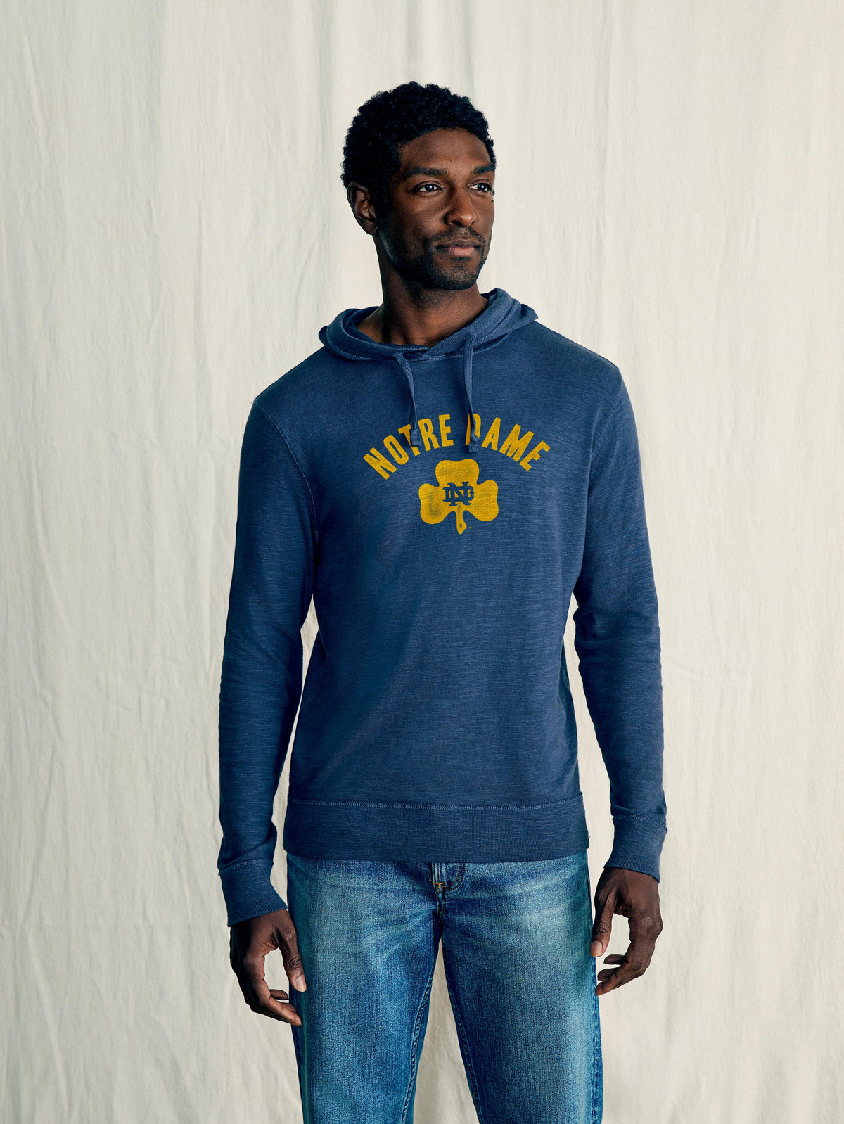A man wearing a blue Notre Dame hoodie and blue jeans, image 1 of 1