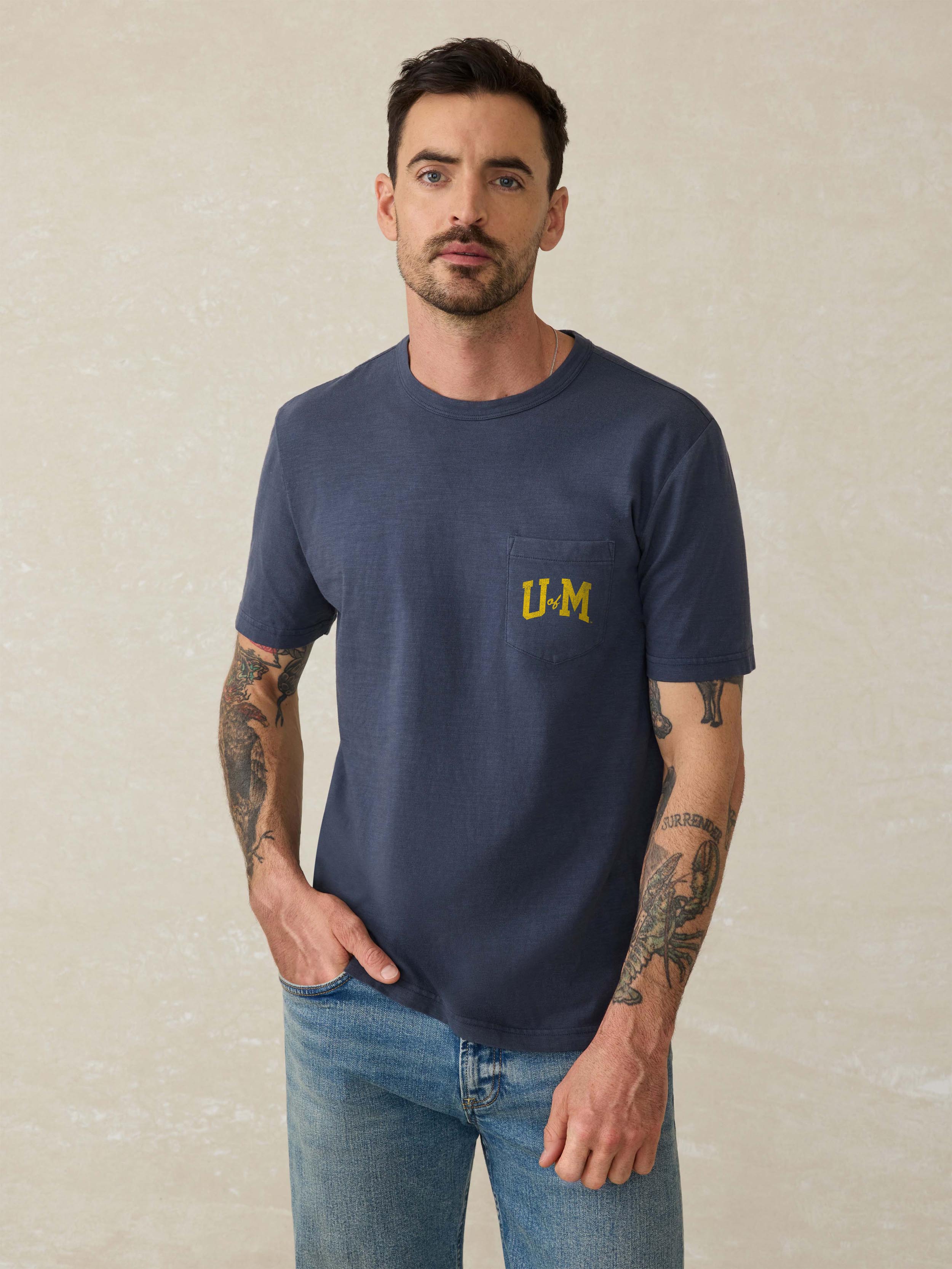 A man wearing a blue University of Michigan tee and blue jeans