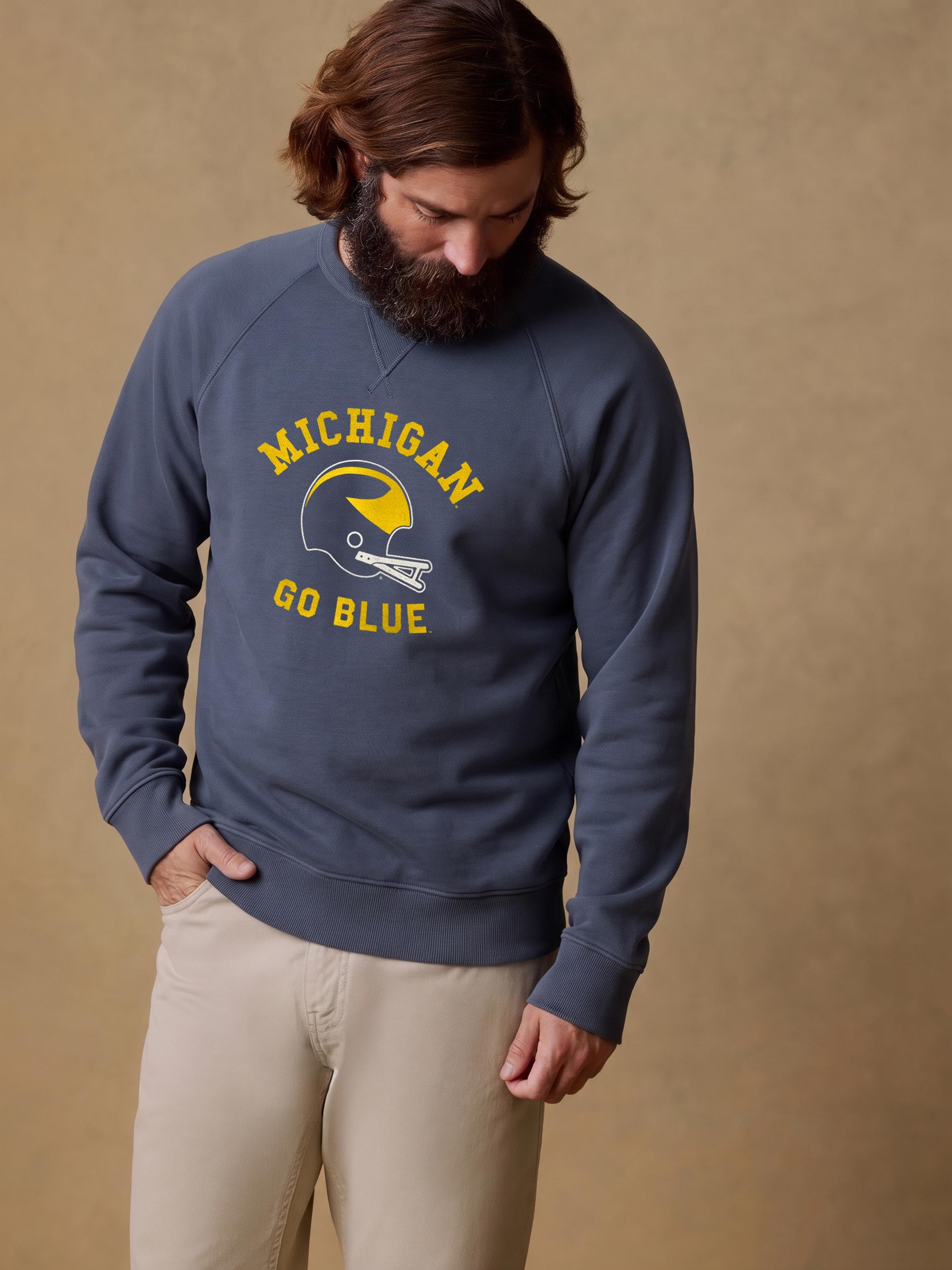 A man wearing a blue University of Michigan crewneck and beige pants
