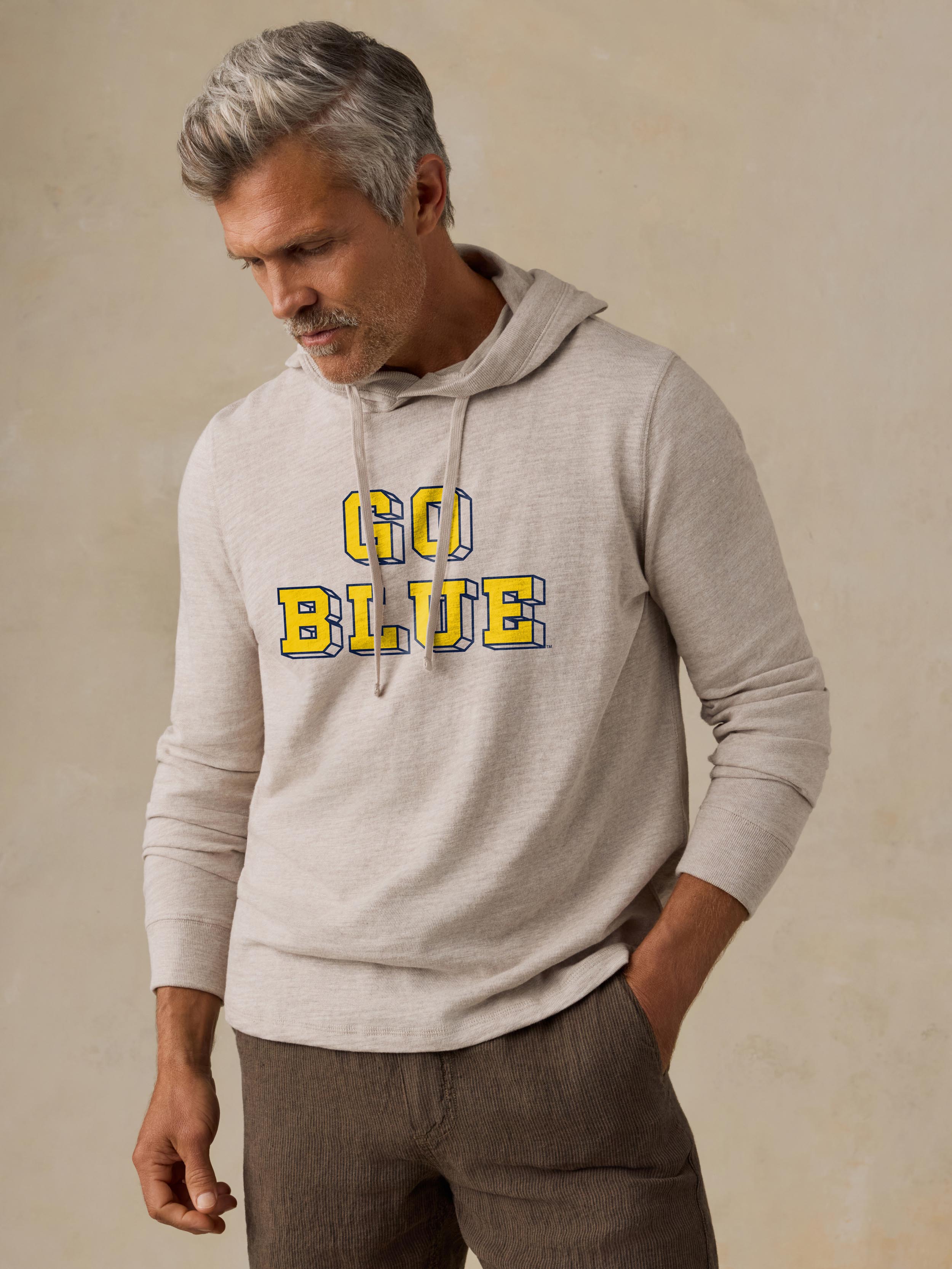 A man wearing a grey University of Michigan hoodie and brown shorts