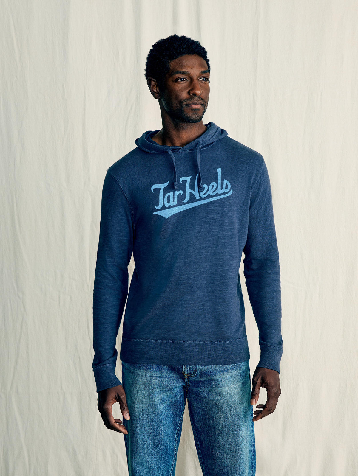 A man wearing a blue University of North Carolina hoodie and blue jeans, image 1 of 1