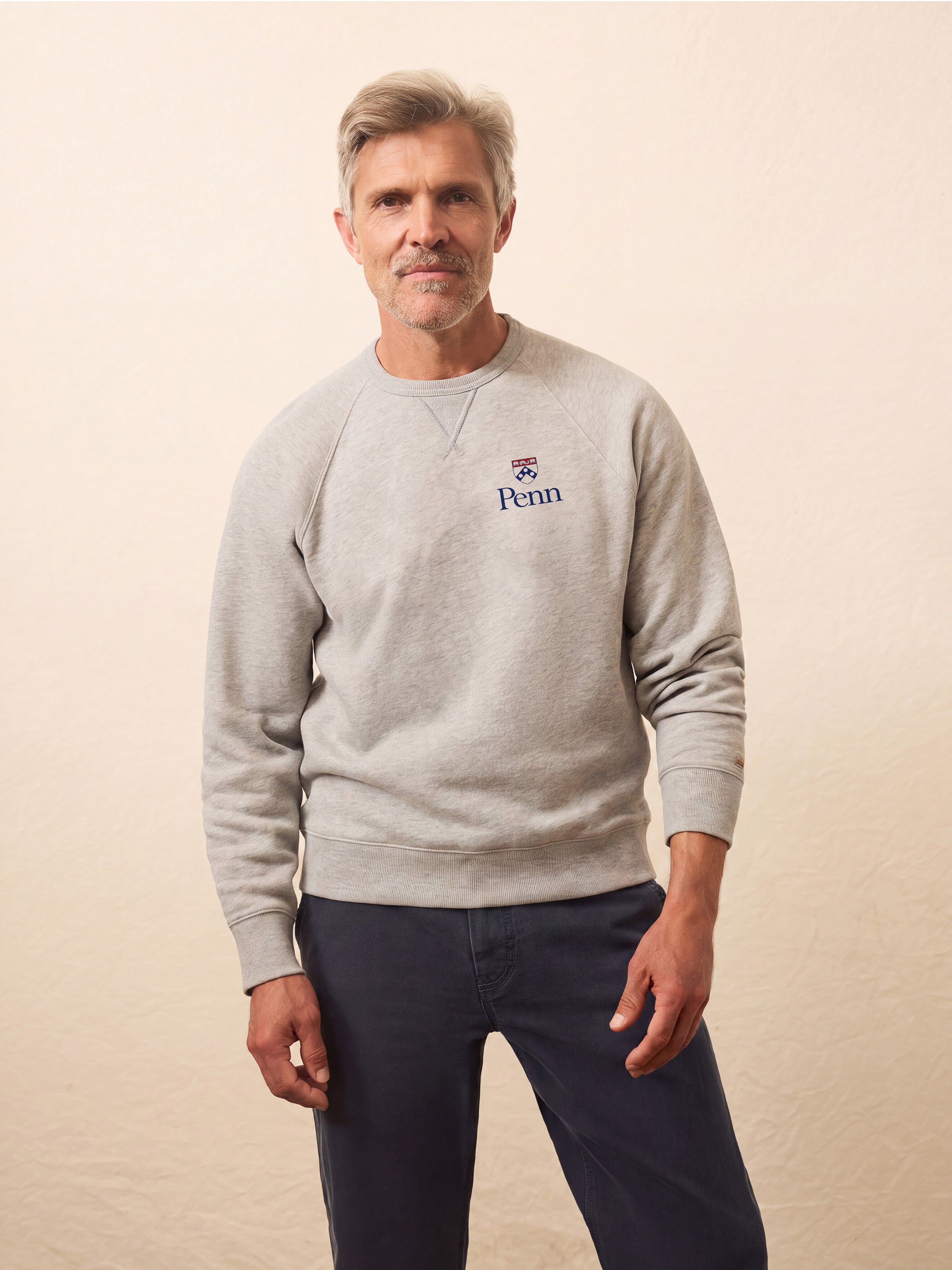 A man wearing a grey University of Pennsylvania crewneck and blue pants