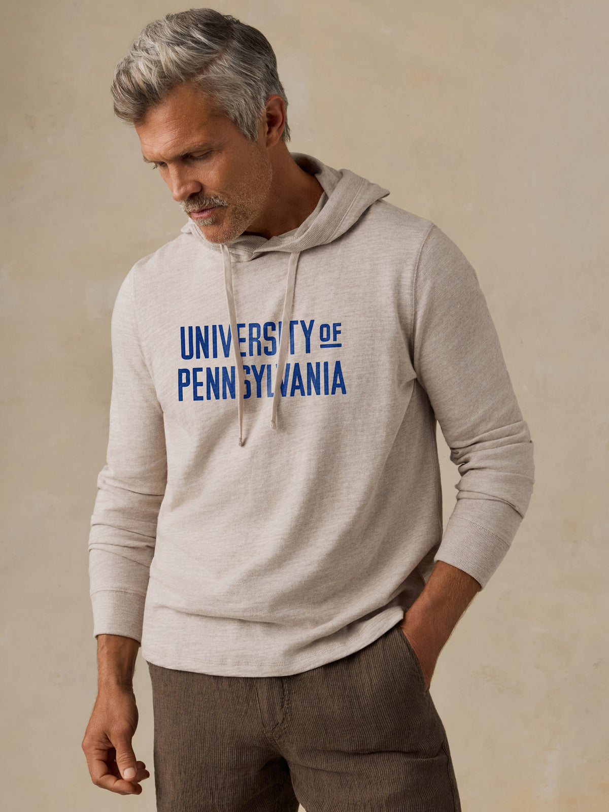 A man wearing a beige UPenn hoodie and brown shorts, image 1 of 1