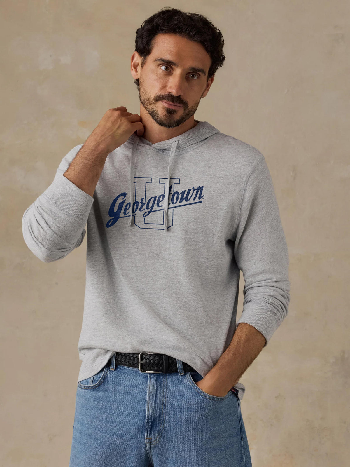 A man wearing a grey Georgetown hoodie and blue jeans, image 1 of 1