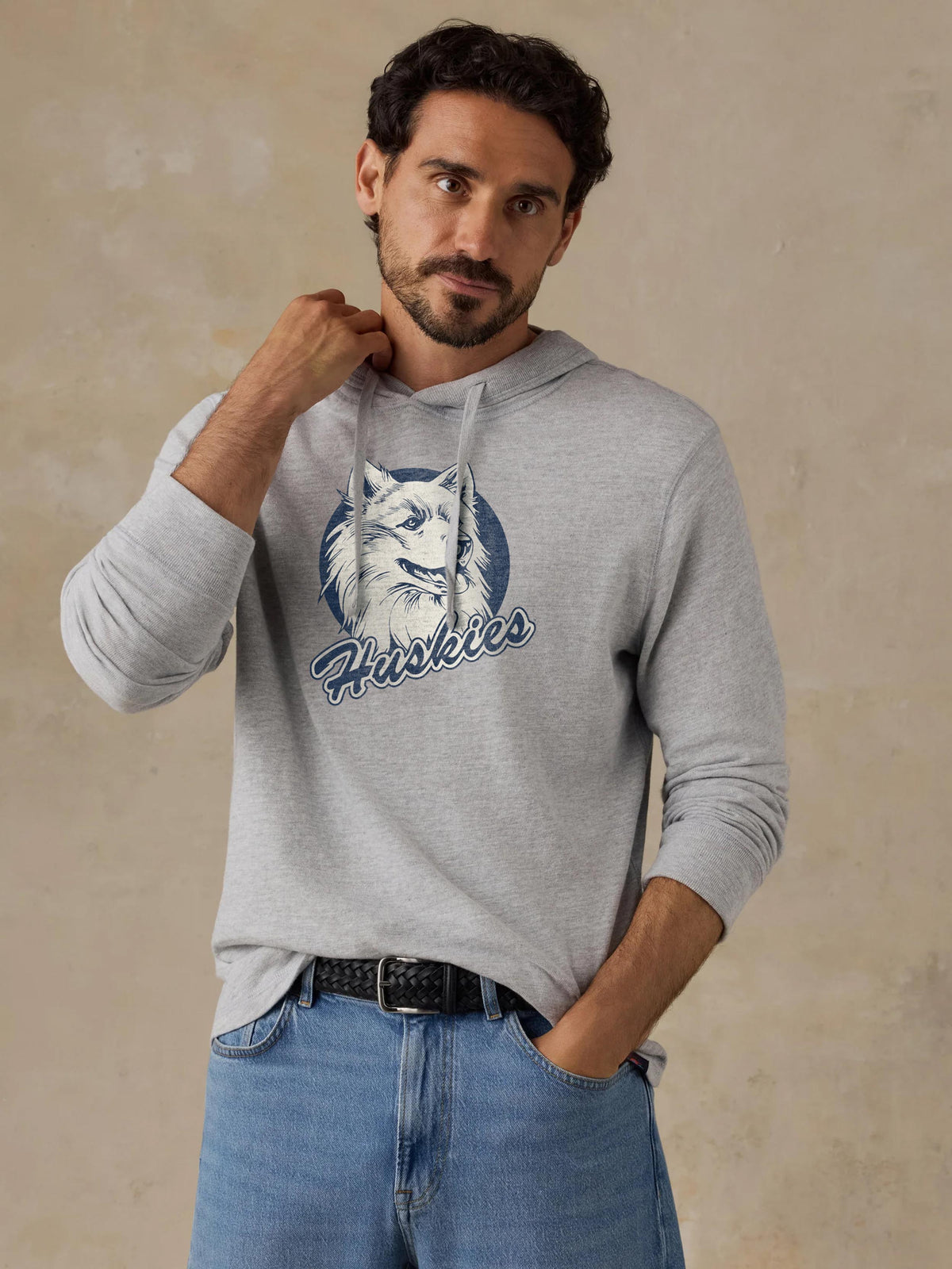 A man wearing a grey UCONN hoodie and blue jeans, image 1 of 1