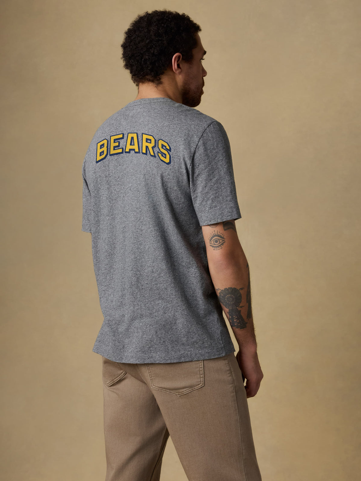 A man viewed from the back wearing a UC Berkeley tee and brown pants, image 2 of 2