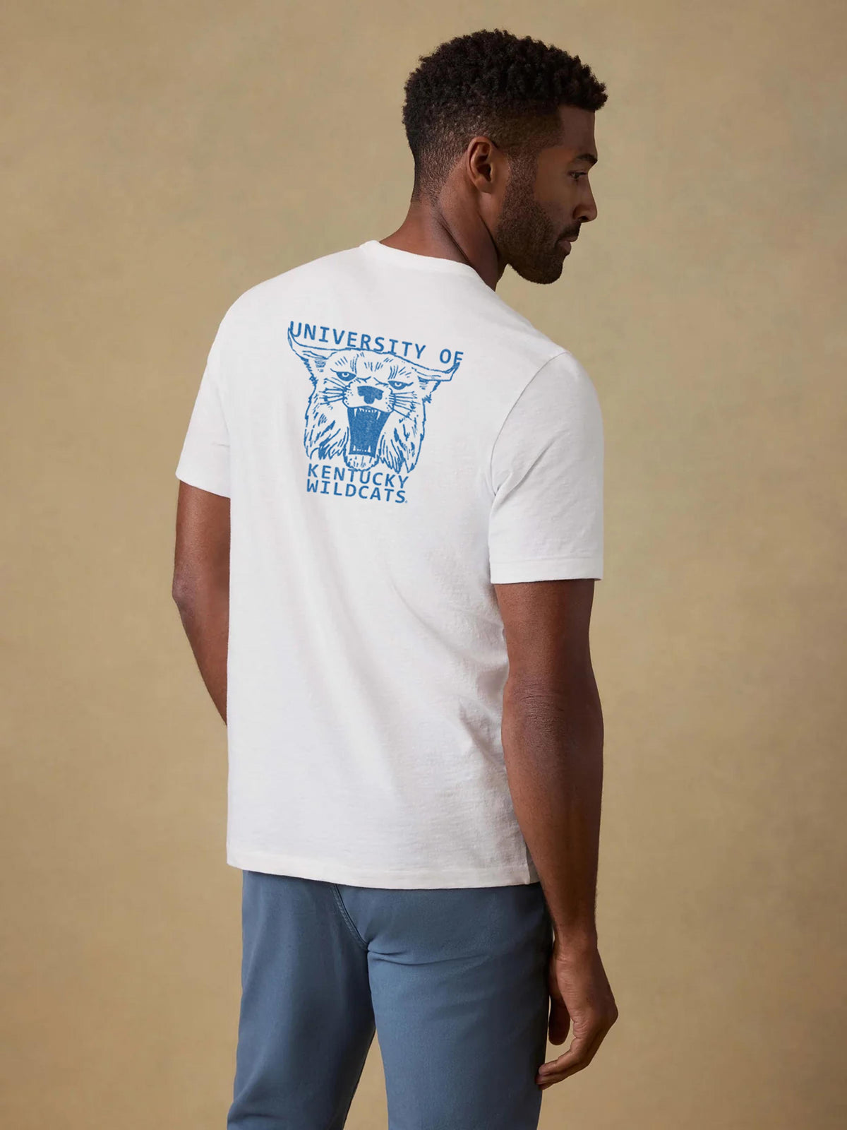 A man viewed from behind wearing a white University of Kentucky tee and blue pants, image 2 of 2