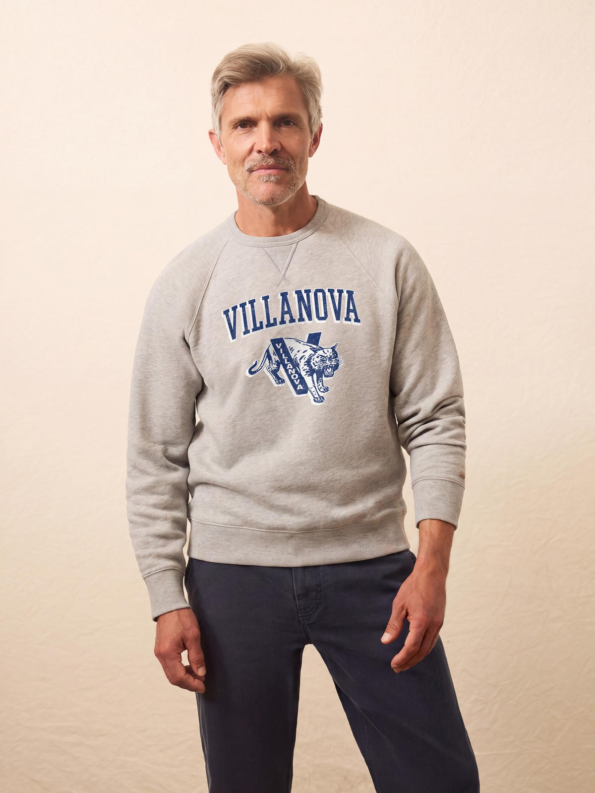 A man wearing a grey Villanova crewneck and blue pants, image 1 of 1