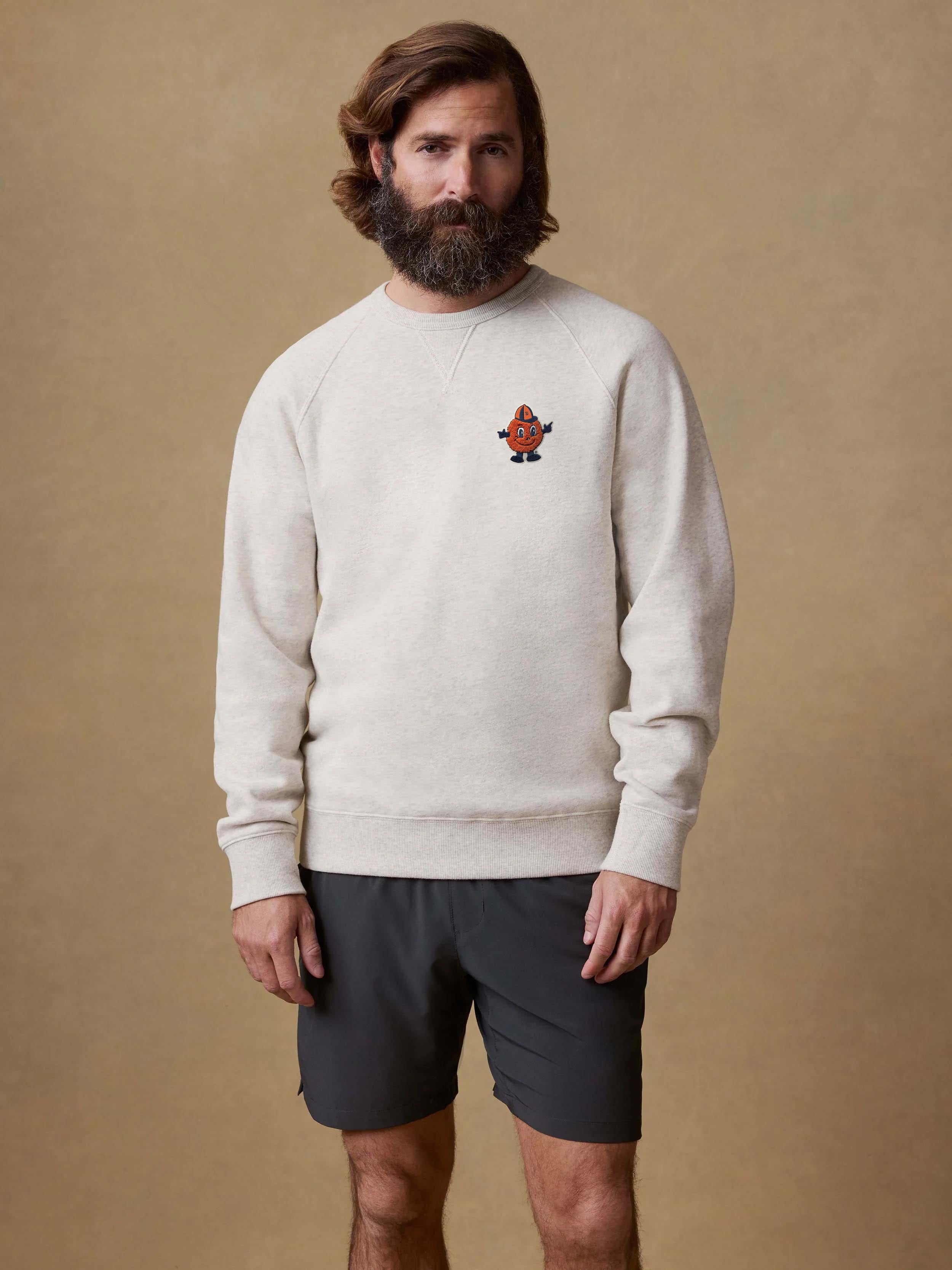 A man wearing a light grey Syracuse crewneck and black shorts