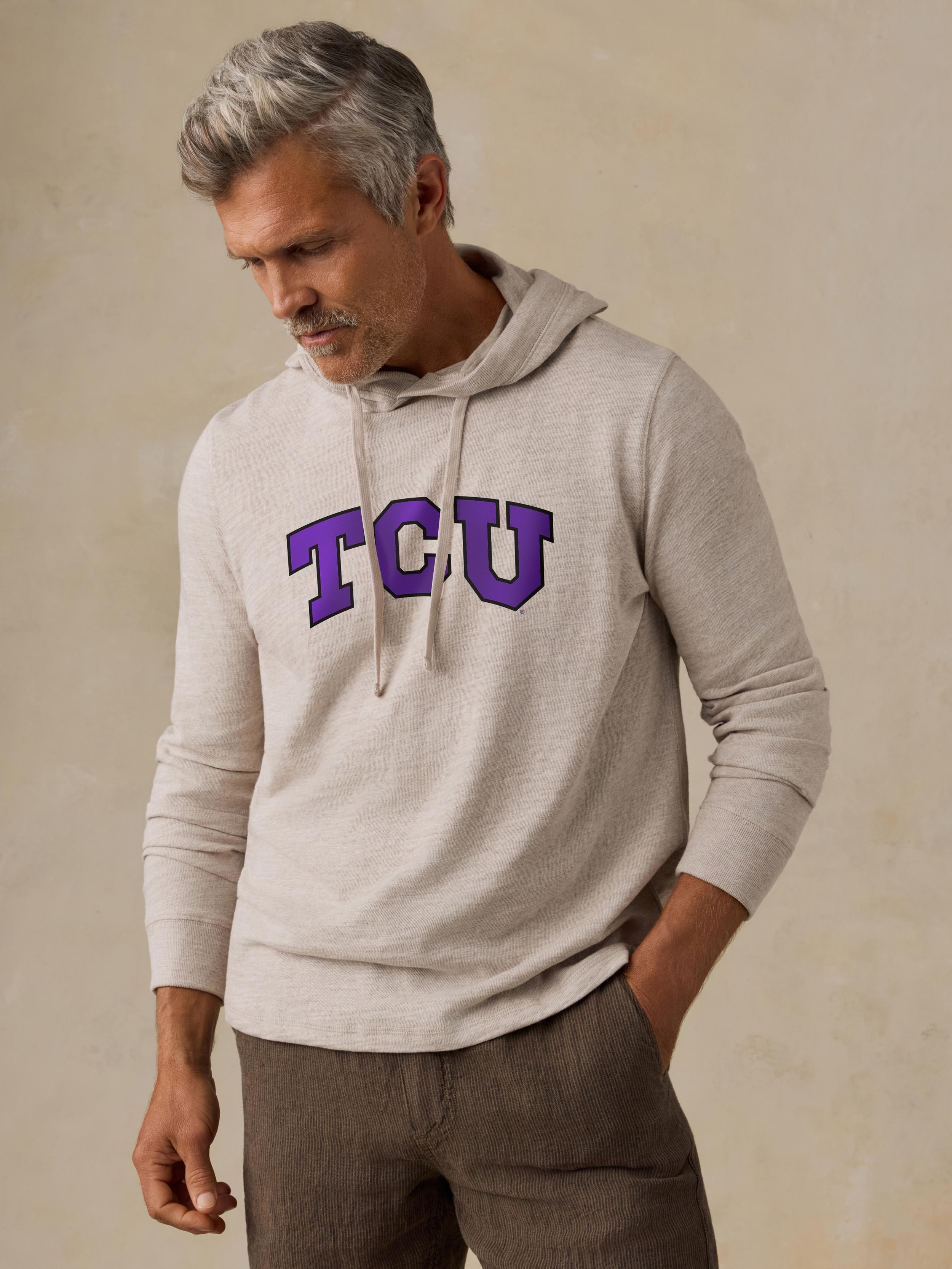 A man wearing a beige TCU hoodie and brown shorts