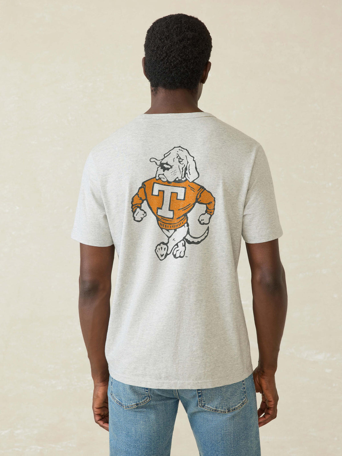 A man viewed from behind wearing a grey University of Tennessee tee and blue jeans, image 2 of 2